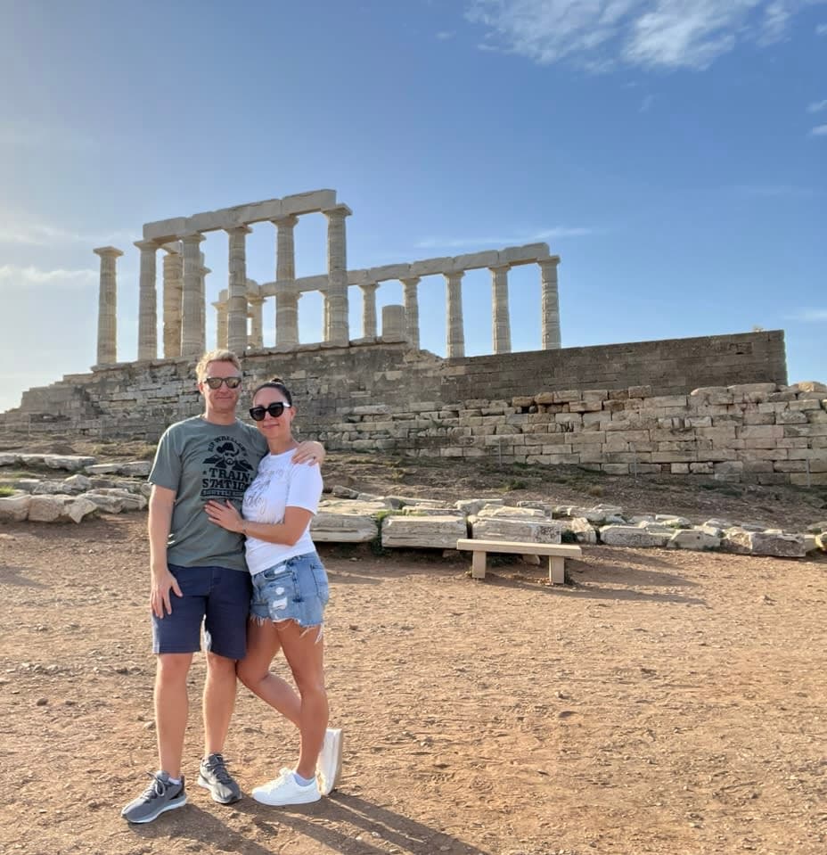 Megan and a man with their arms around each other in front of ruins in Greece.