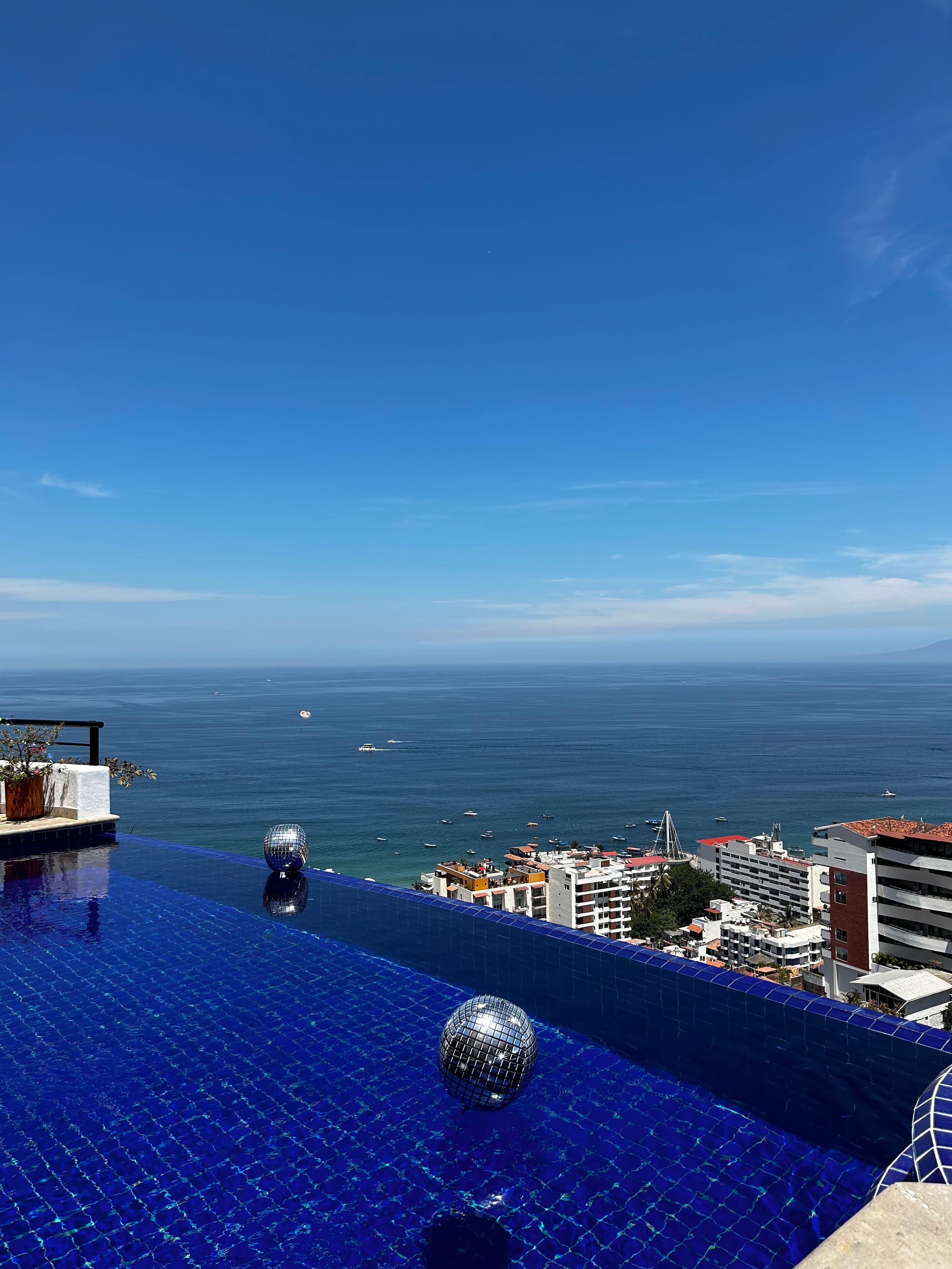 A photo of a blue-tiled infinity pool overlooking a town on the seaside.