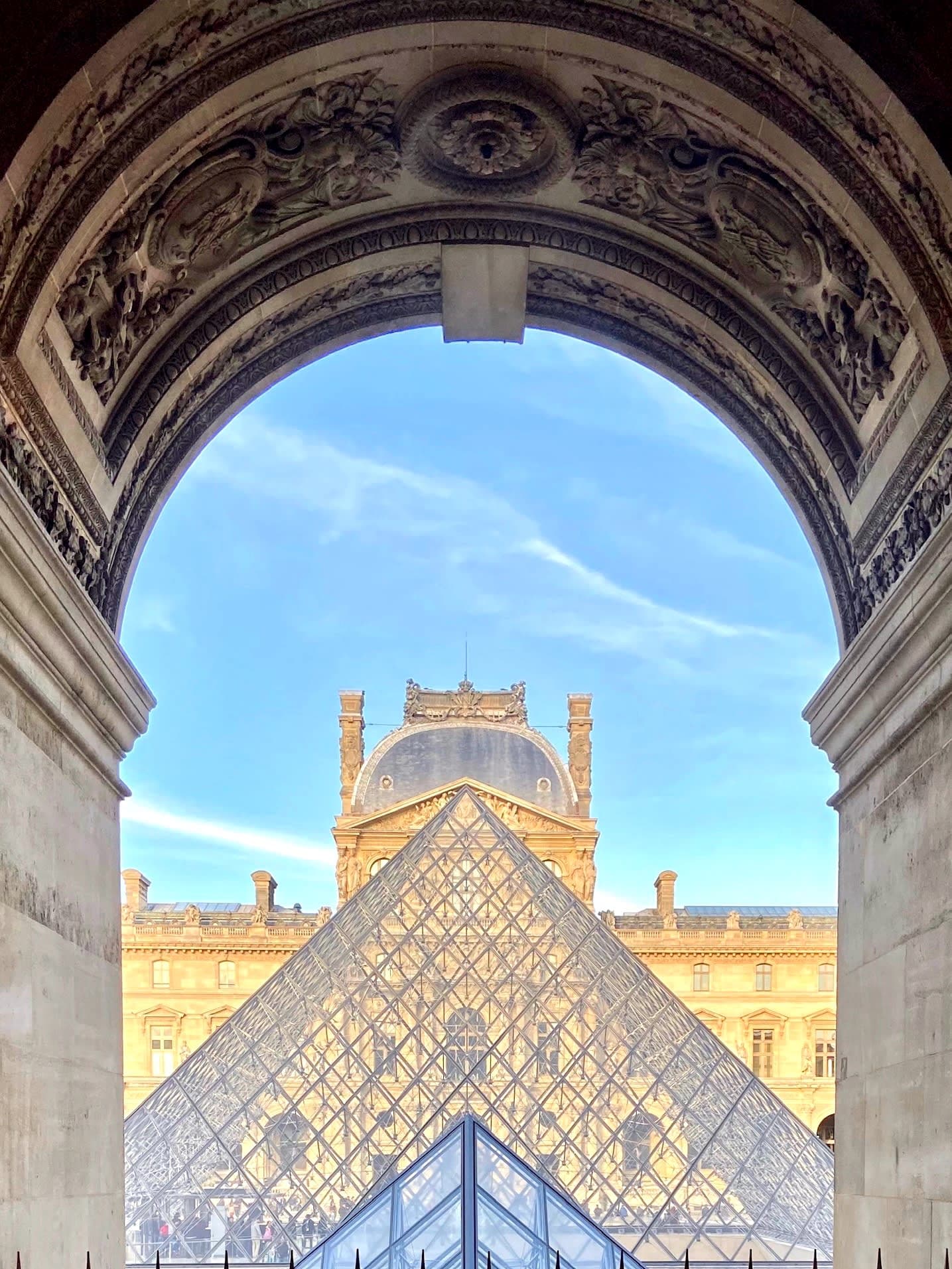 View of The Louvre Pyramid from an arched hallway entrance with stone carvings