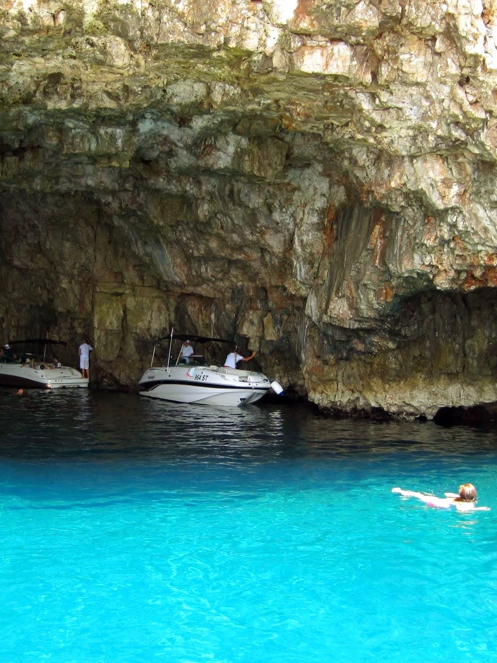 View of a sea cave in Croatia, boats are anchored under the cave and people are swimming in the sea