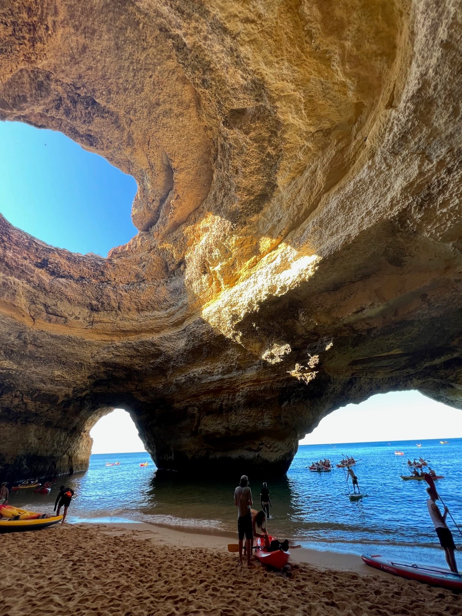 Isabella standing under a large rock formation that opens to the sky next to the ocean.