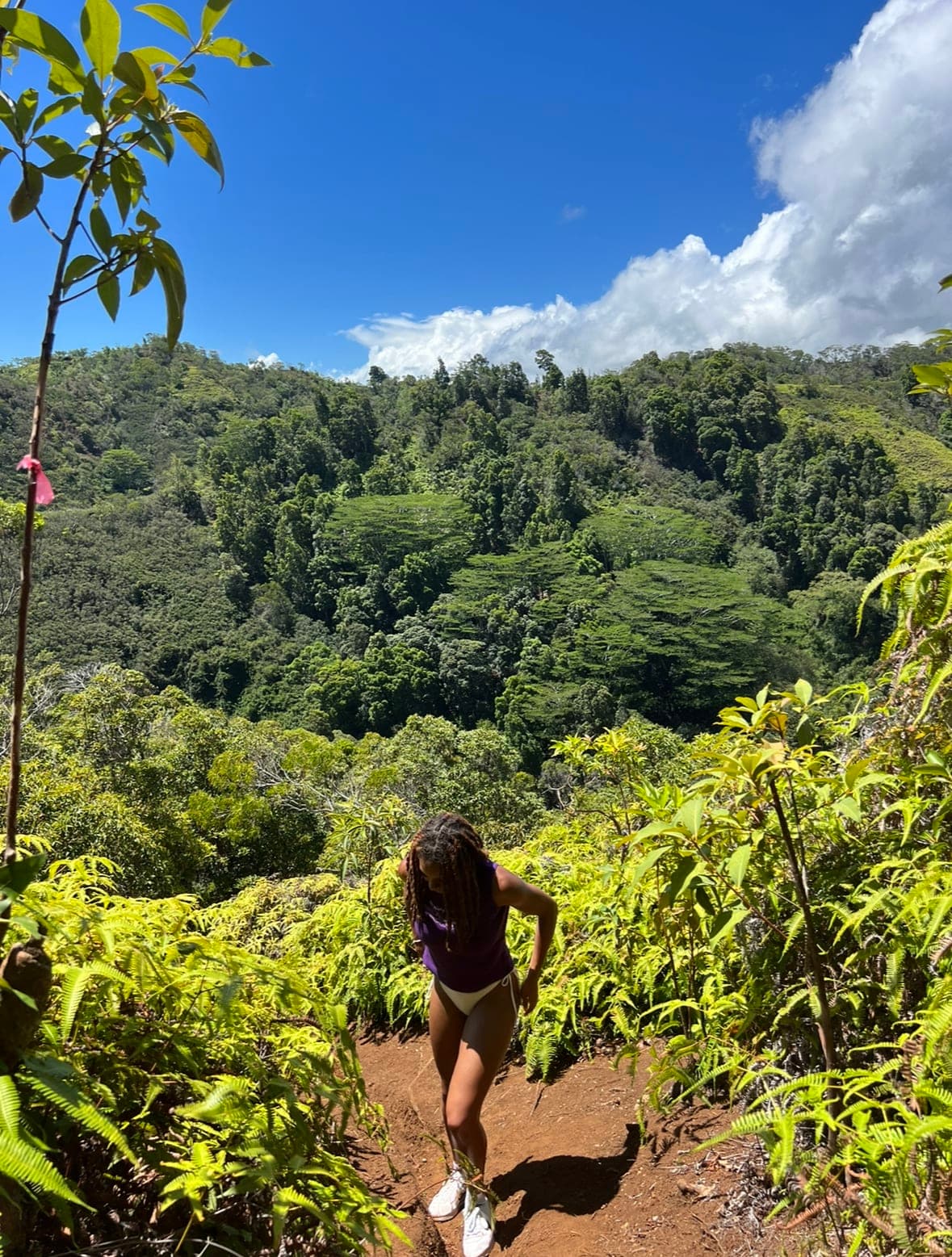 A girl hiking on a dirt path through a lush forest.