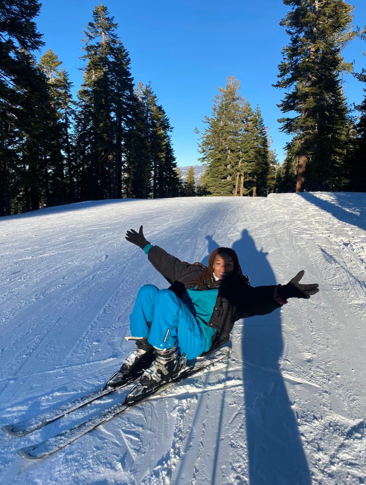Sydney, in snow clothes lying on a path covered in snow and lined with pine trees on either side.
