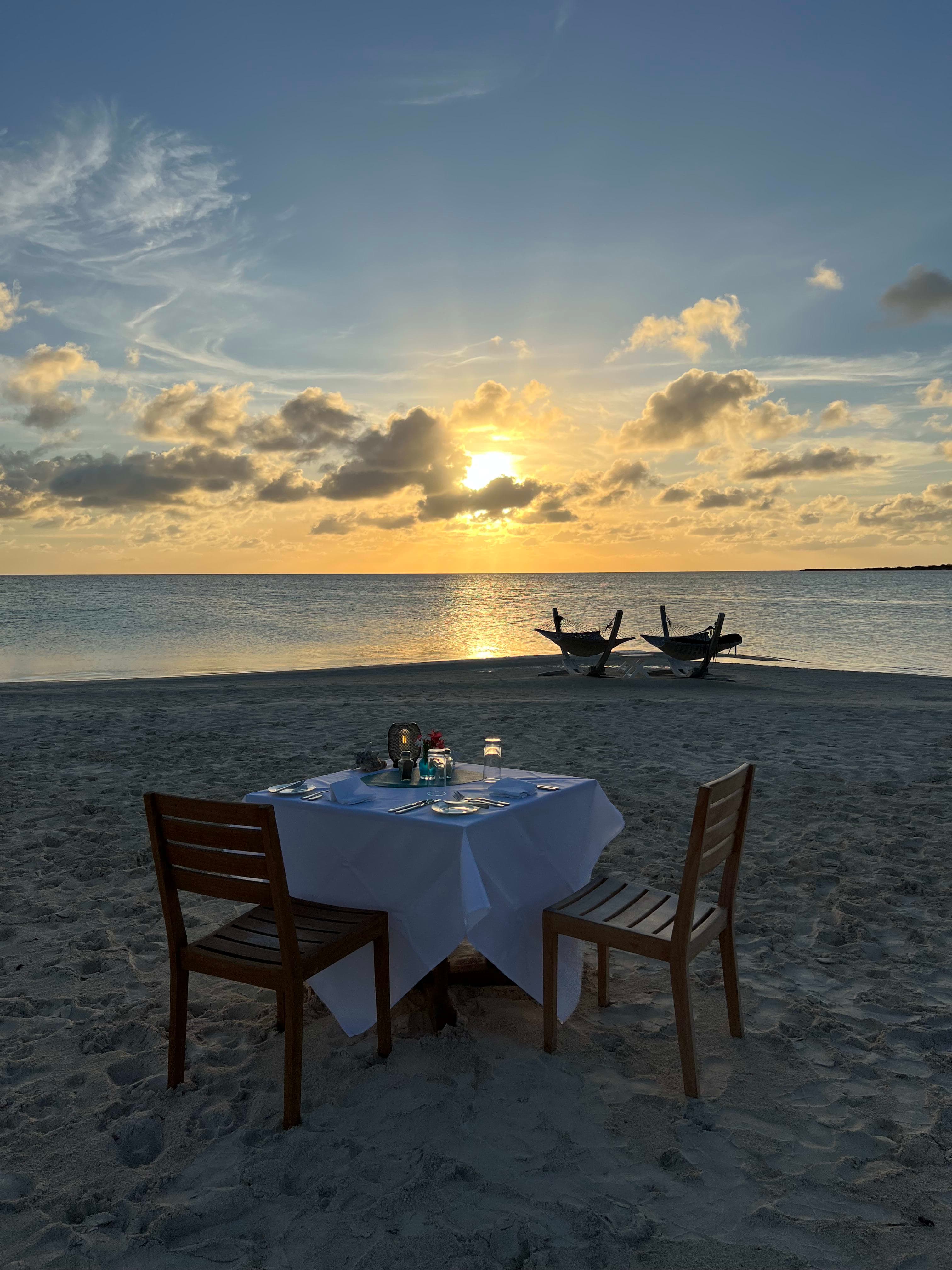 Two empty chairs and a dinner table on the beach at sunset