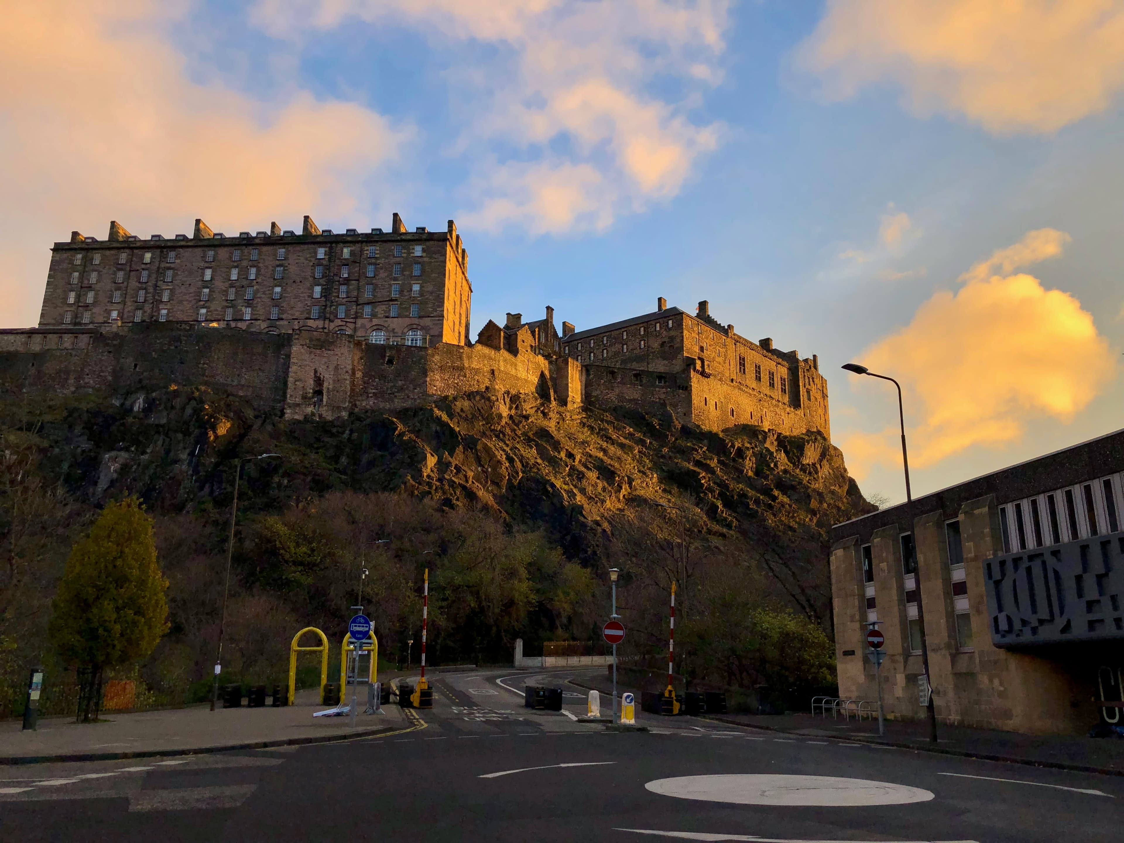 Beautiful view of Edinburgh Castle from the road at sunset with orange clouds and blue skies
