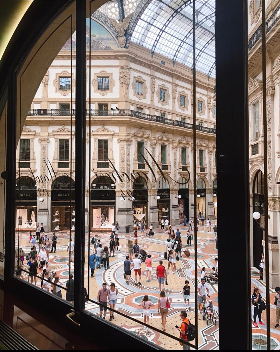View through a window of an ornate indoor shopping mall full of people