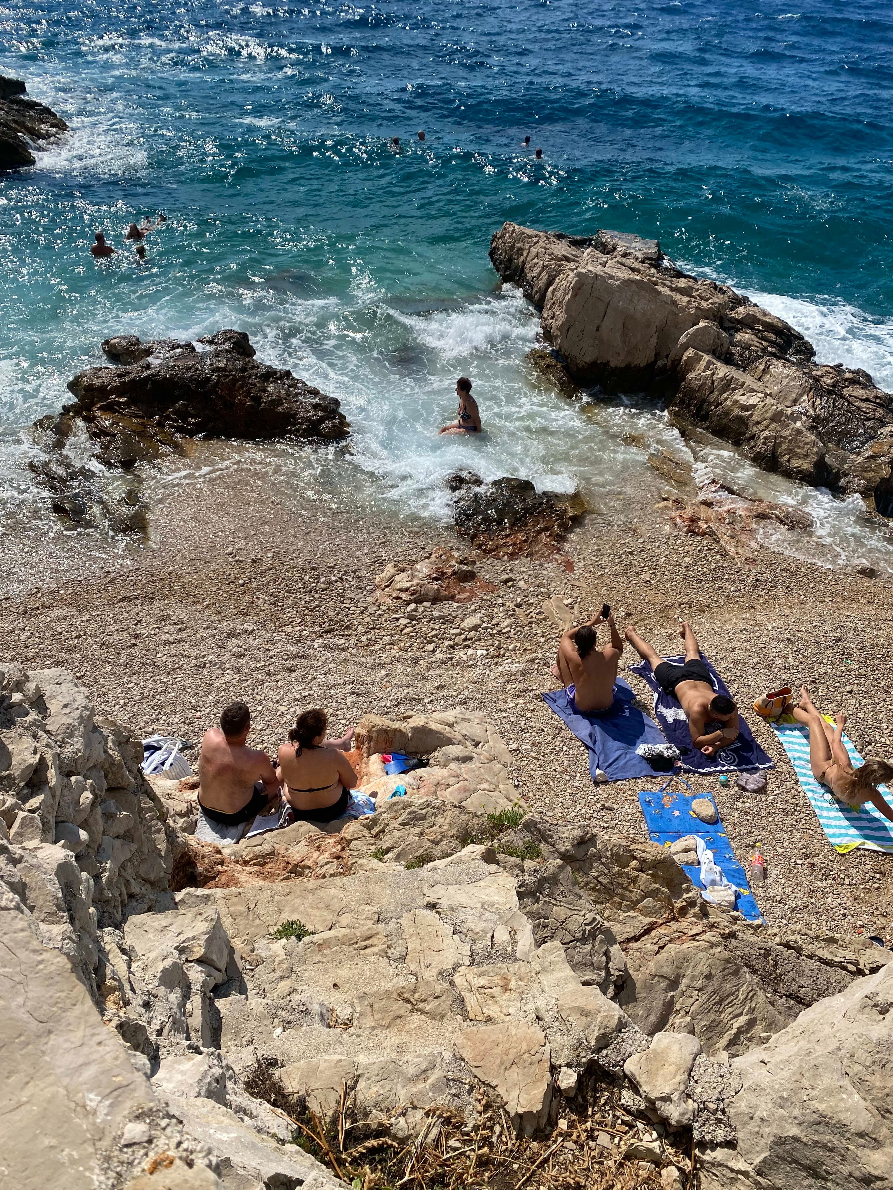 Aerial view of people sunbathing on towels on a rocky cliff stretching out to the ocean