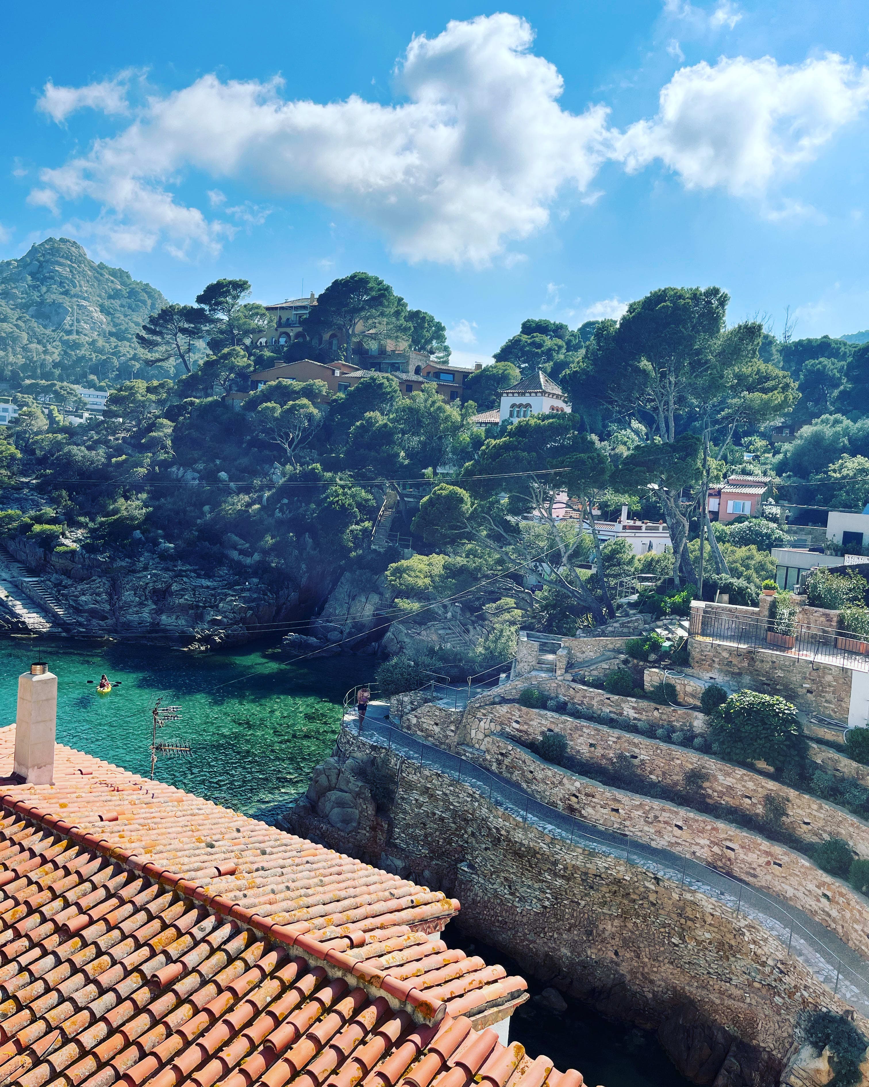 Beautiful view of an orange-roofed building overlooking Costa Brava next to lush greenery and stone walls