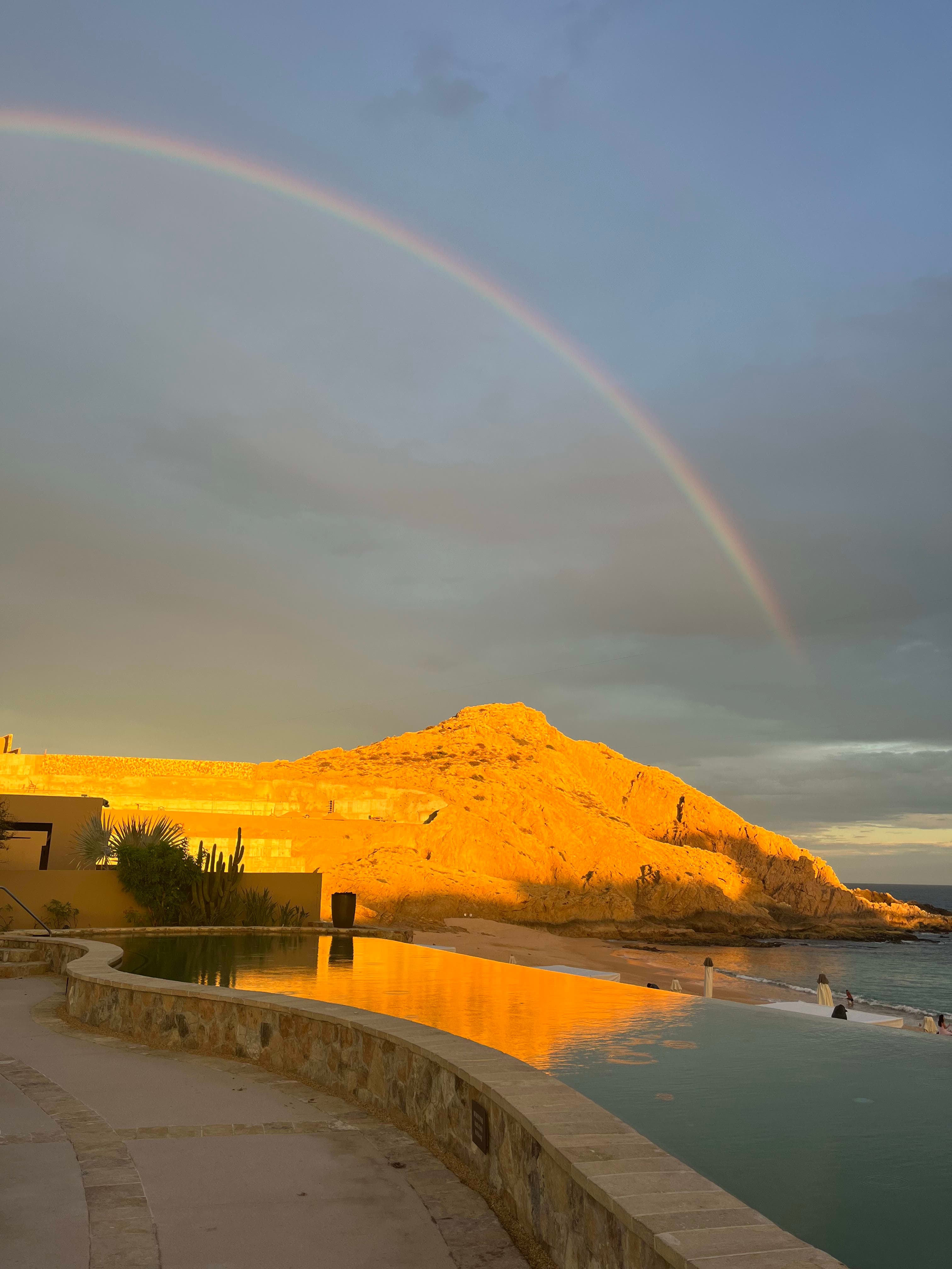Beautiful view of rainbow stretching over a mountain alongside the sea