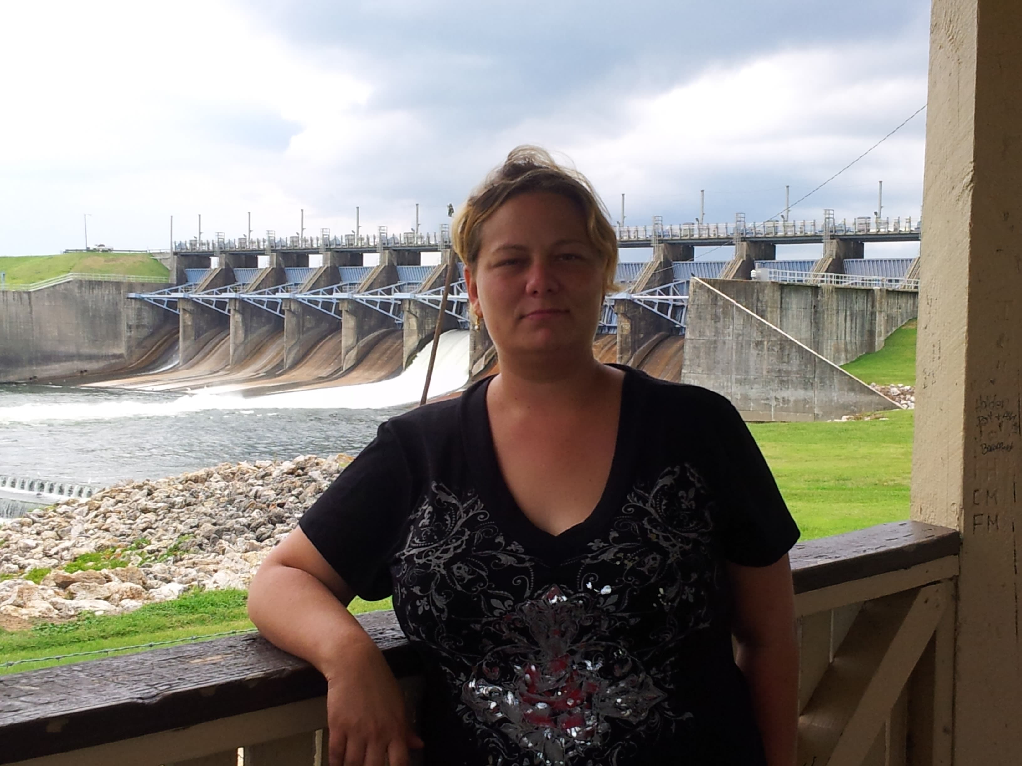 Picture of Wendy wearing a bejeweled t-shirt and posing in front of Lake Livingston Dam on a cloudy day
