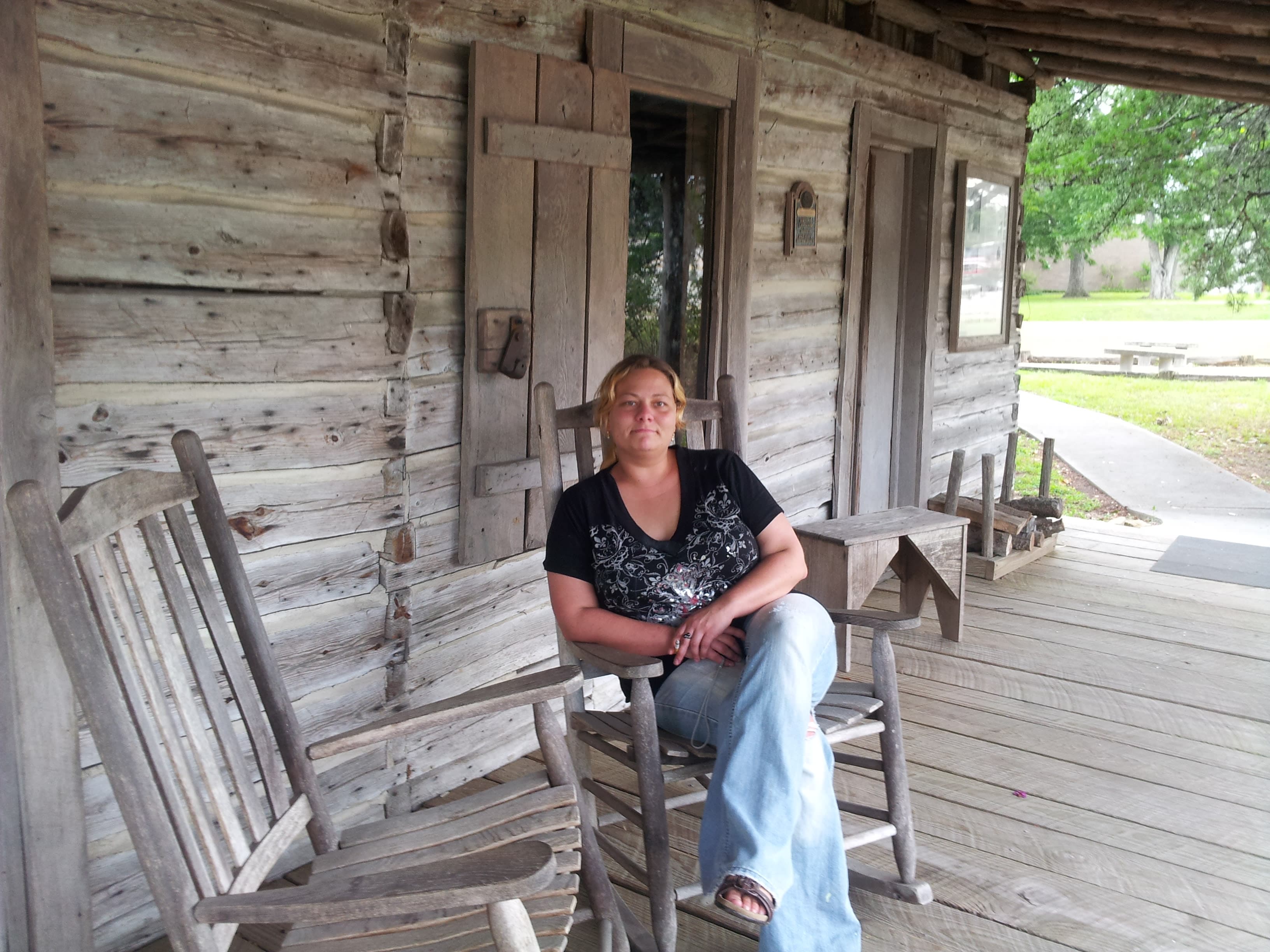 Picture of Wendy sitting on a wooden rocking chair on the porch of a wooden house