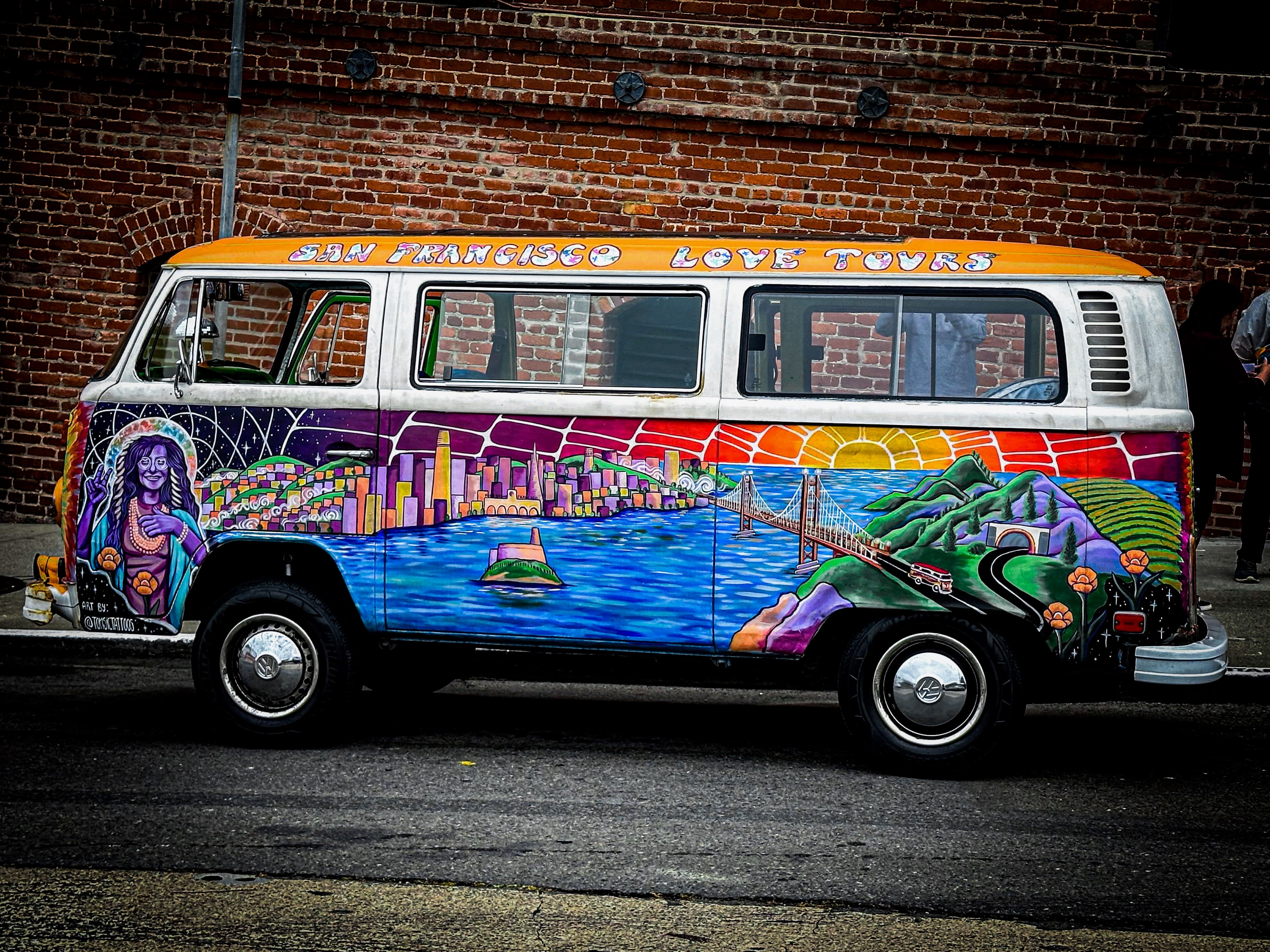 Picture of a colorfully painted old-fashioned van parked on a road in front of a brick wall
