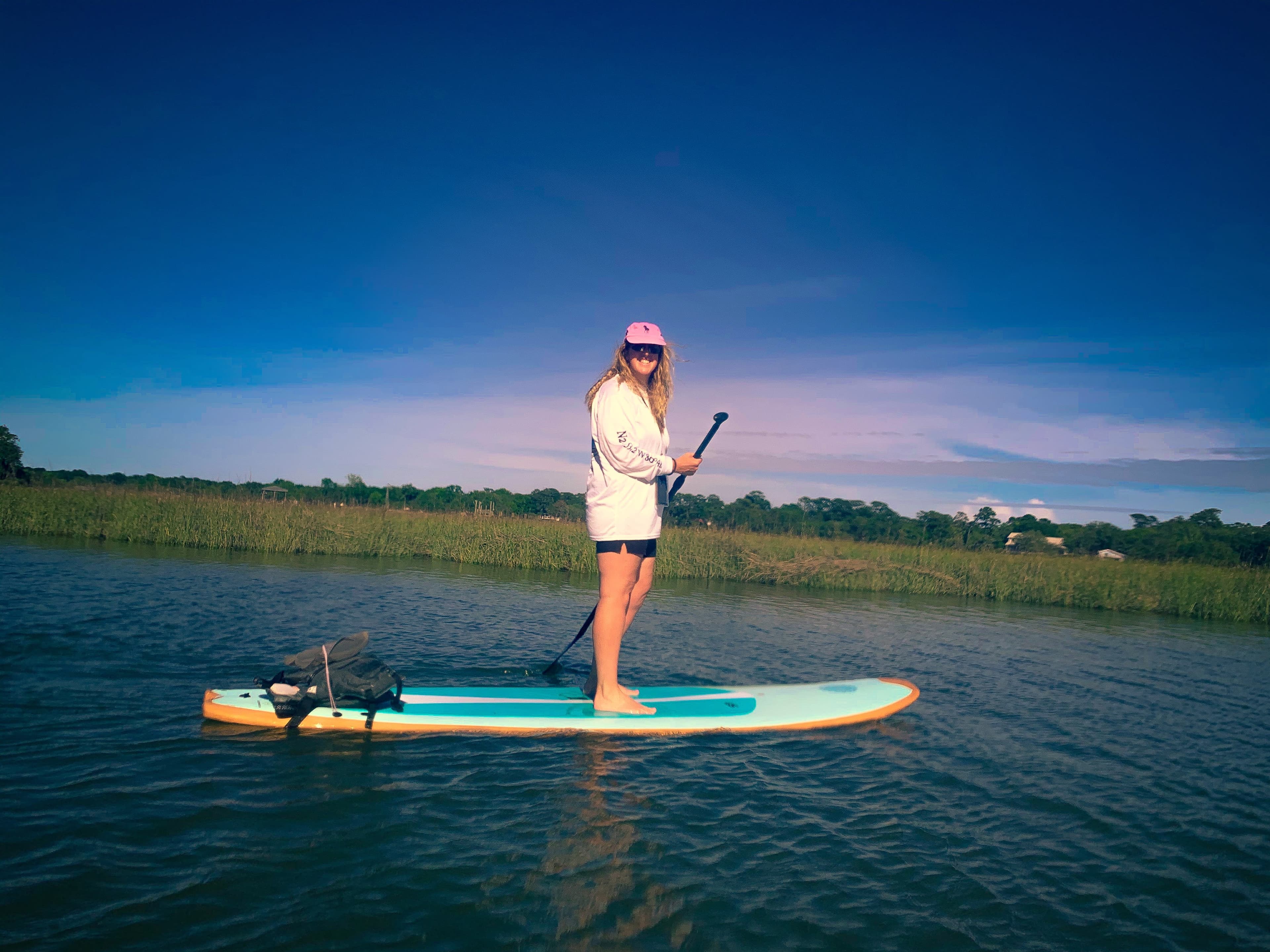 Picture of Sarah wearing a pink hat and holding an oar while balancing on a stand up paddle board
