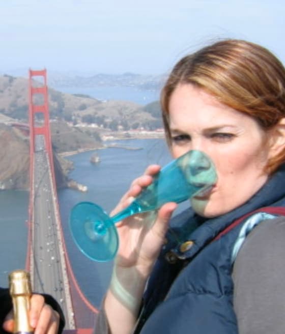 Laura drinking out of a blue plastic champagne flute with a view of the Golden Gate bridge in the background below.