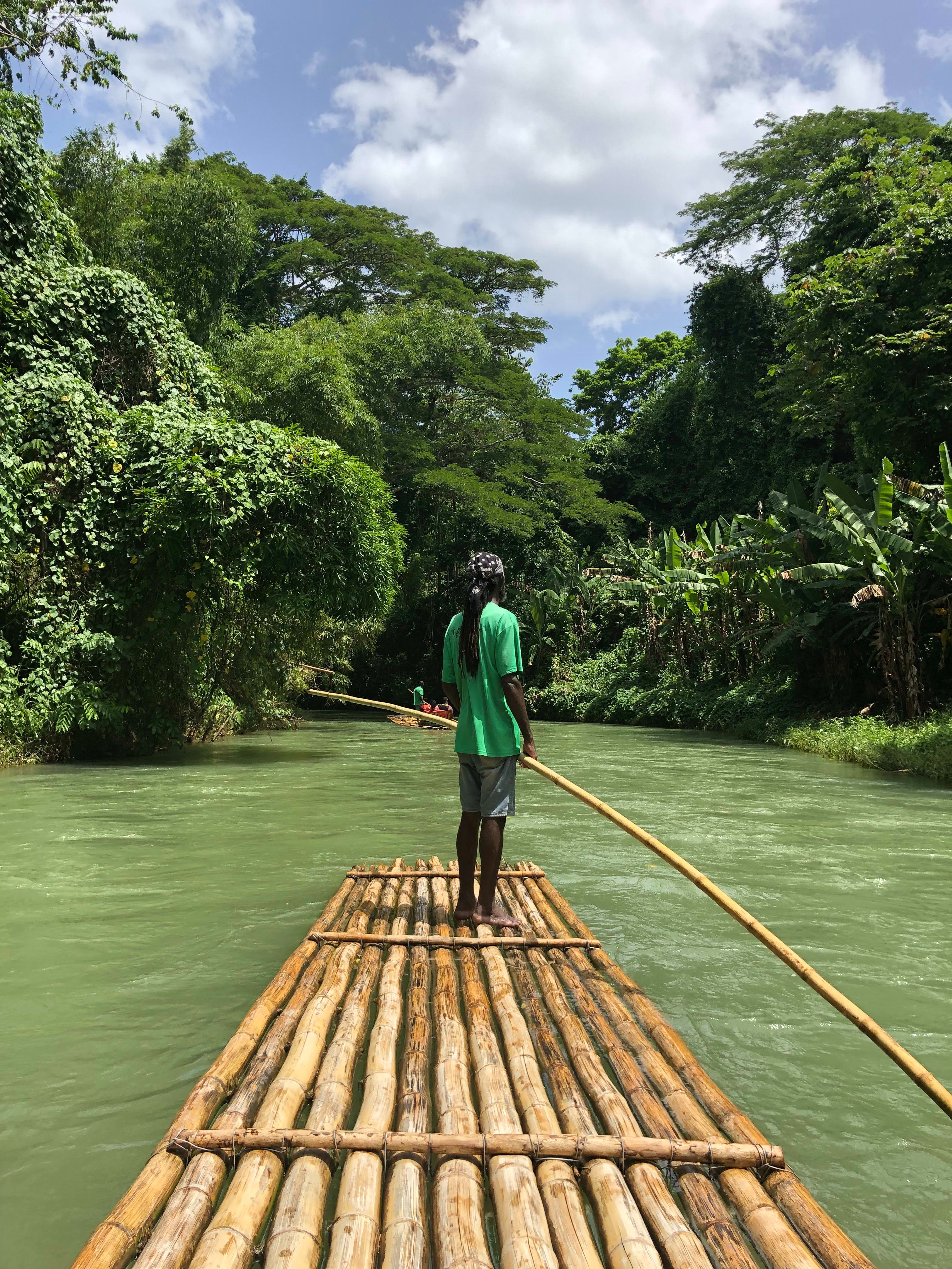 Picture of Dajah holding an oar on a wooden raft sailing the Martha Brae River surrounded by lush trees