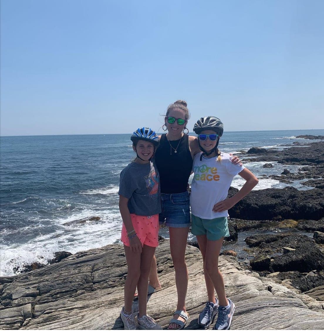 Picture of Jill posing with her daughters on a cliff with the ocean in the background on a sunny day