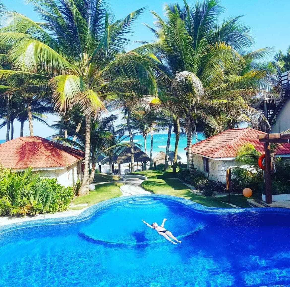 Picture of Jill floating on her back in a large pool with palm trees and the ocean in the background