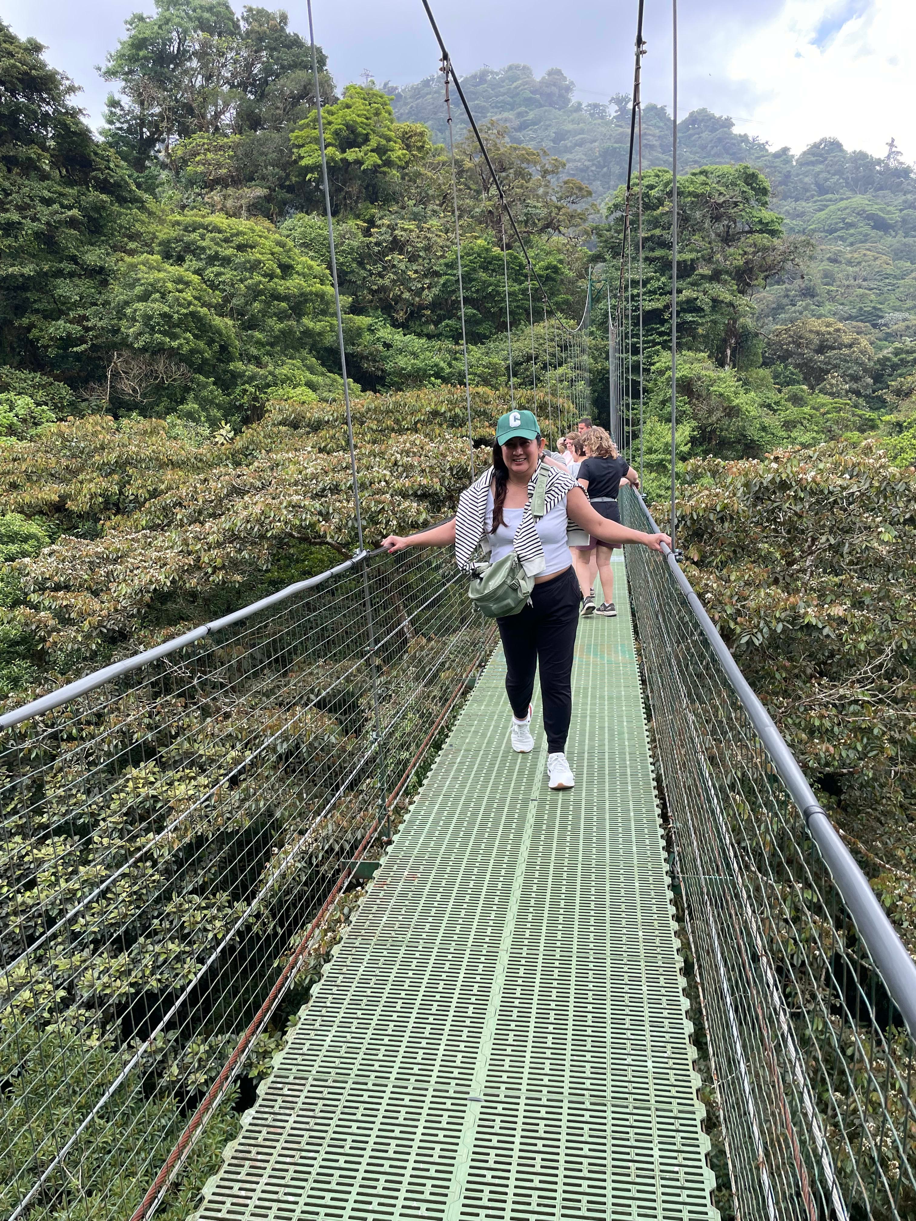 Picture of Hazel walking on a narrow suspension bridge through the jungle on a cloudy day
