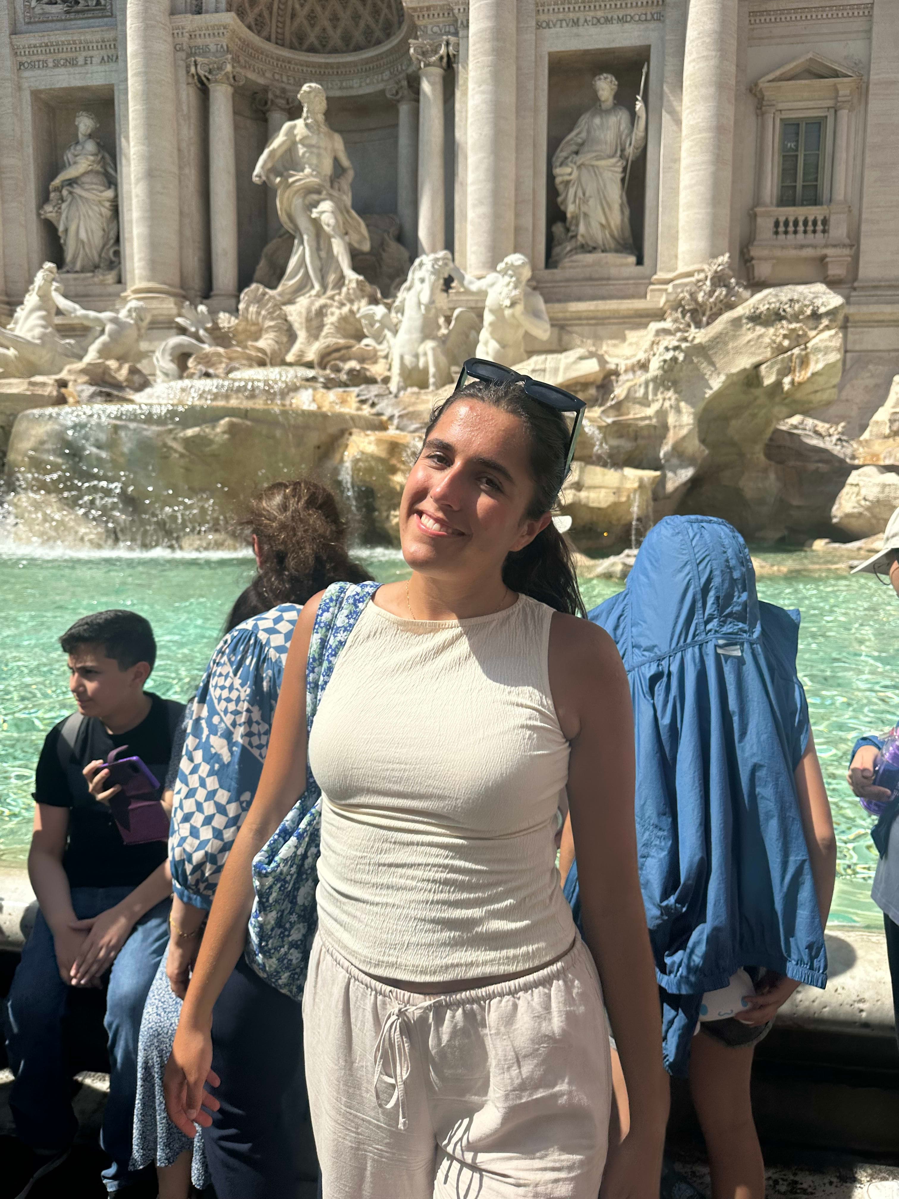 Avery posing for a photo in a white outfit in front of the Trevi Fountain