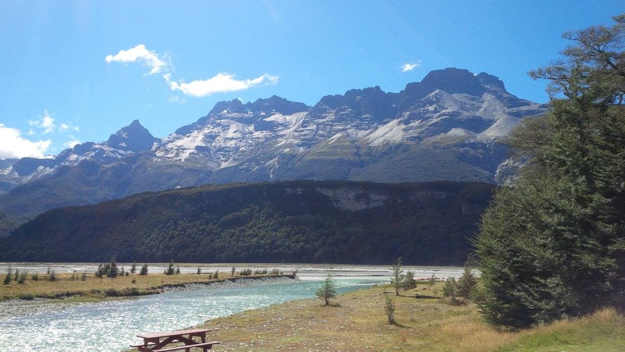 Beautiful view of the Dart River on a nice sunny day surrounded by greenery and the view of snow covered mountains in the background