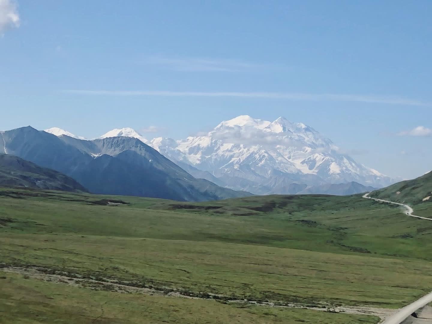 Beautiful view of a vast green field on a clear day with huge snowy mountains in the distance