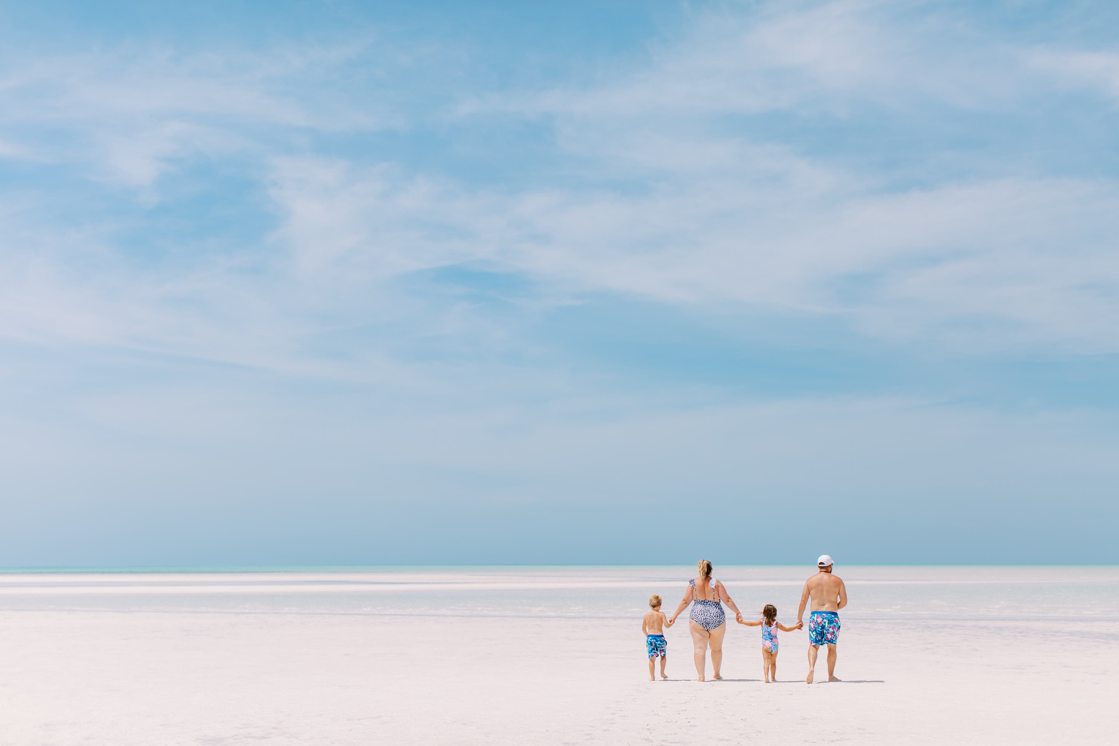 A photo of a family on an empty, white sand beach on a slightly cloudy day.