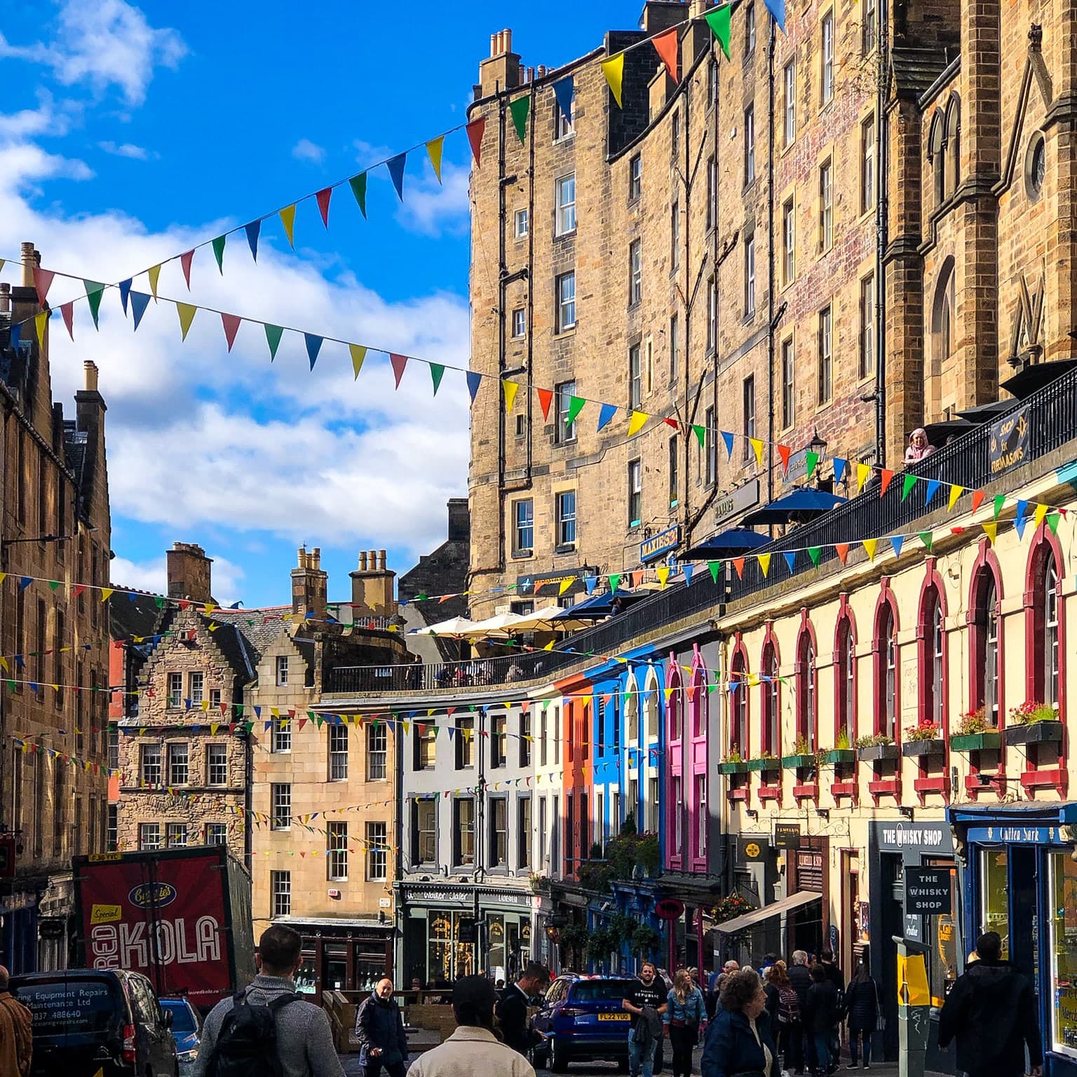 A medieval city street with tall buildings and colorful flags.