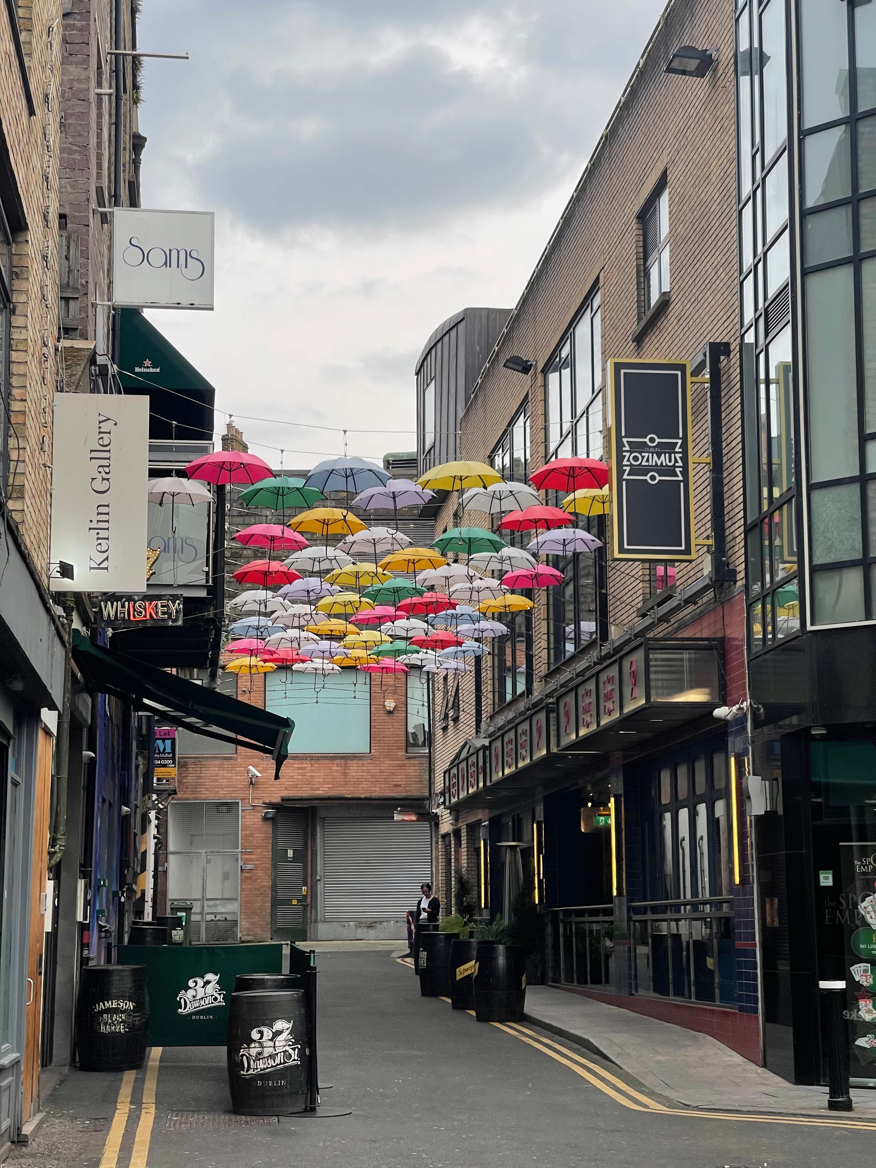 Picture of an empty narrow street with many colorful umbrellas hanging over in between buildings