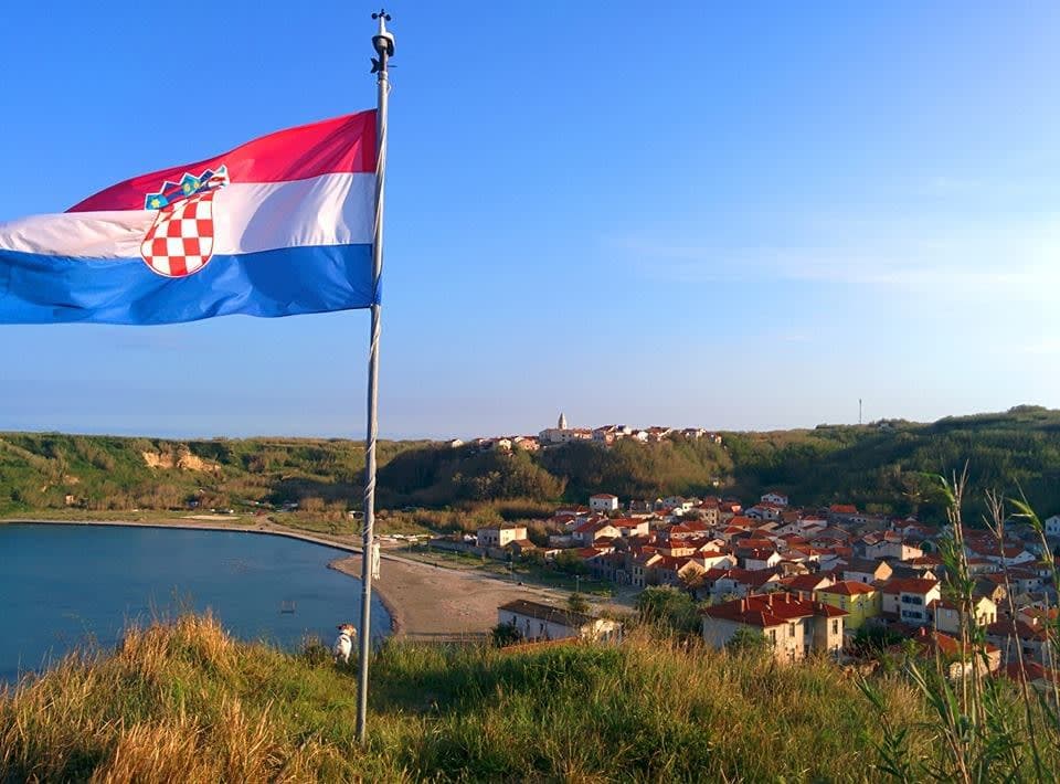 View of the Croatian flag flying above a beautiful bay and sunny coastline