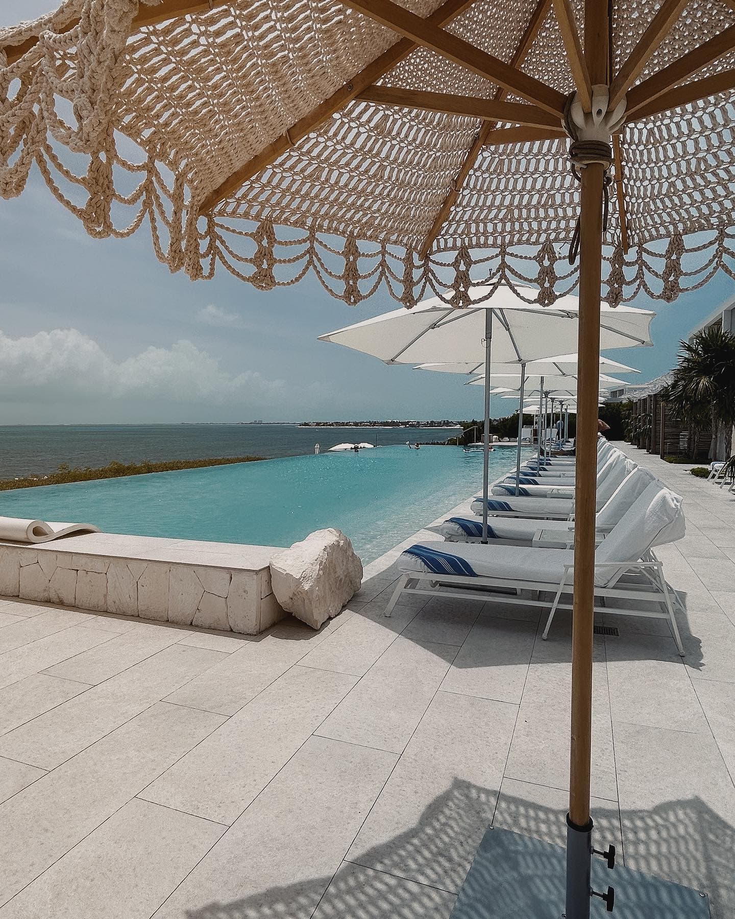 An infinity pool with white lounge chairs and umbrellas overlooking the beach.