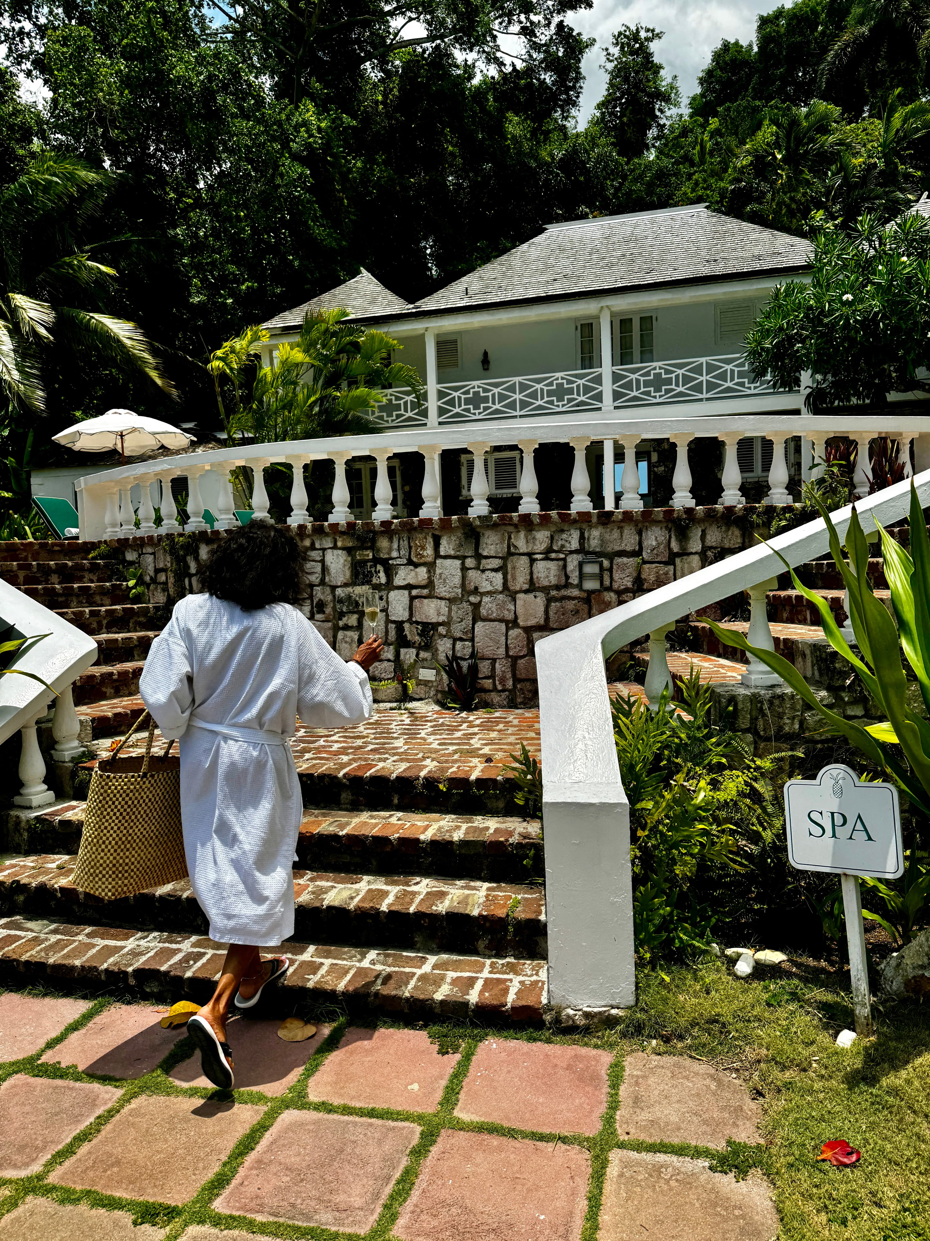 Peta in a white robe holding a bag and a drink in hand walking towards stone stairs