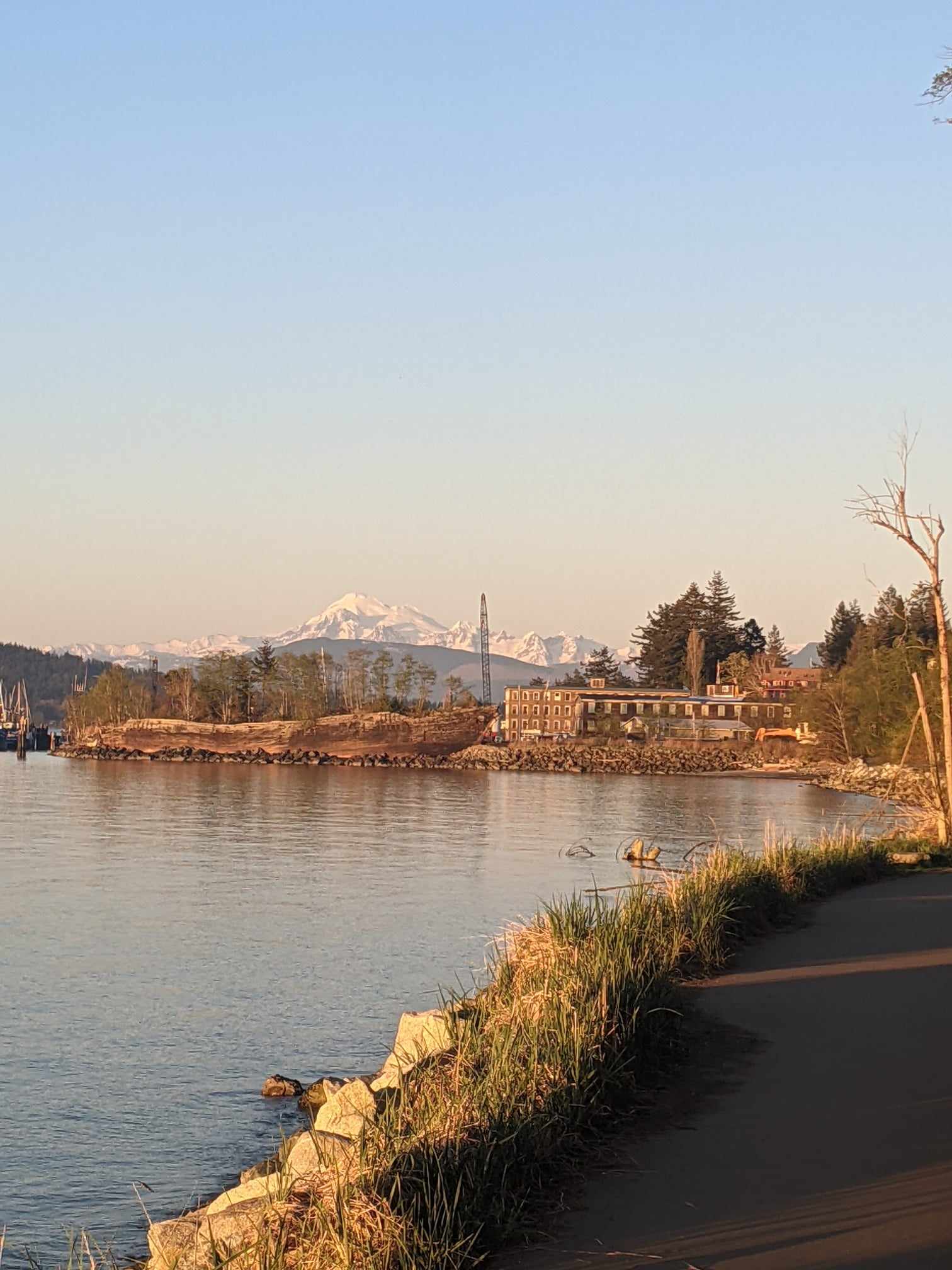 Photo of a building by the lake at the golden hour with snow capped peaks visible far away