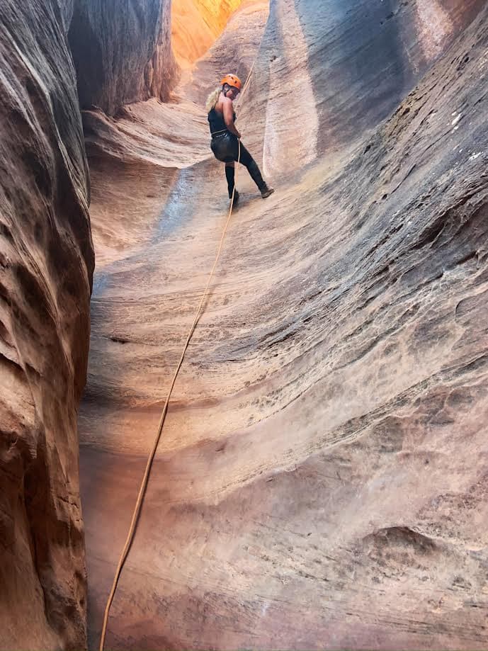 Brianna wearing a helmet while rock climbing a steep incline in Zion National Park