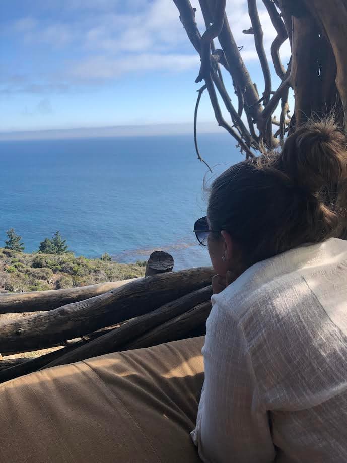 Brianna wearing a white shirt and laying on a sofa looking at the beautiful view of the sea on a clear day