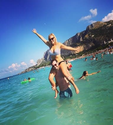 Picture of Kenny holding his girlfriend on his shoulders while in shallow water at the beach