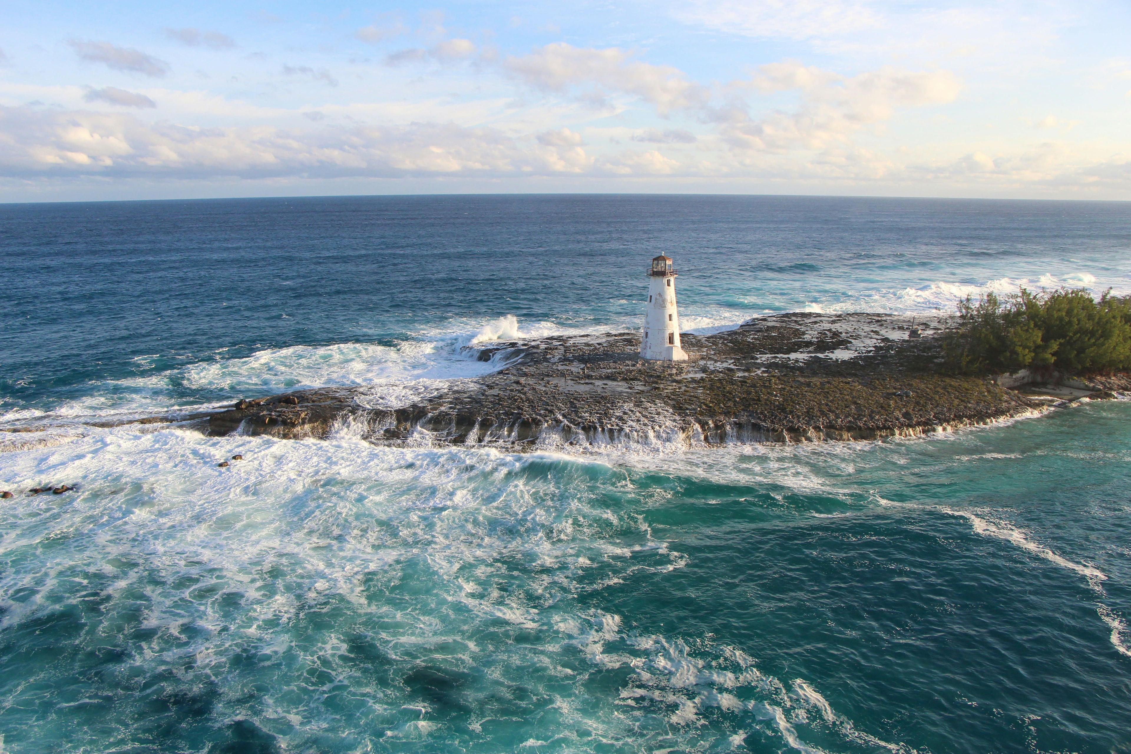 Aerial shot of a white lighthouse on a rocky peninsula with ocean waves crashing ashore