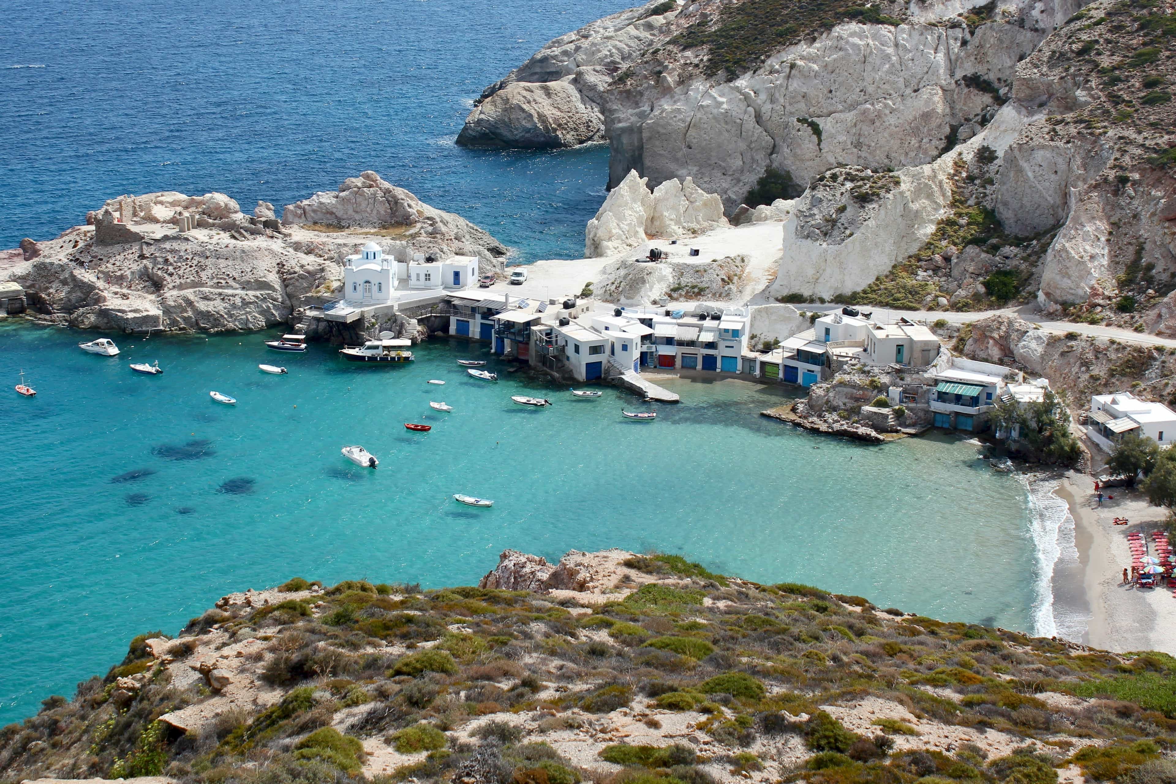 An aerial view of a picturesque coastline with whitewashed buildings and white cliffs, surrounded by turquoise ocean with boats