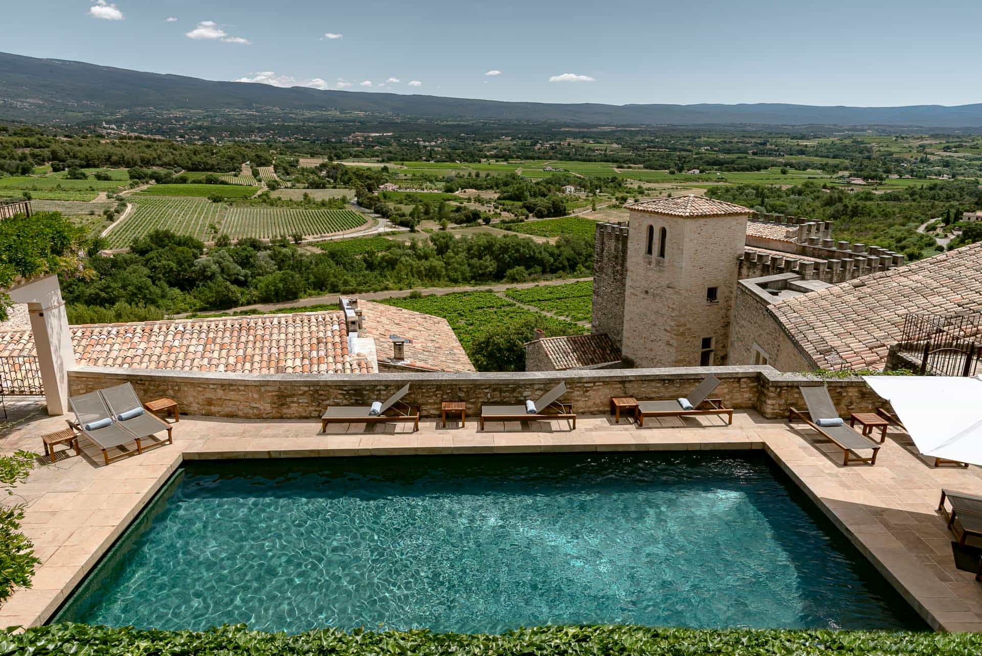 10 Instagram-Worthy Hotel Pools to Visit in 2026 Aerial view of a rooftop pool on a restored tan stone building with green landscape behind