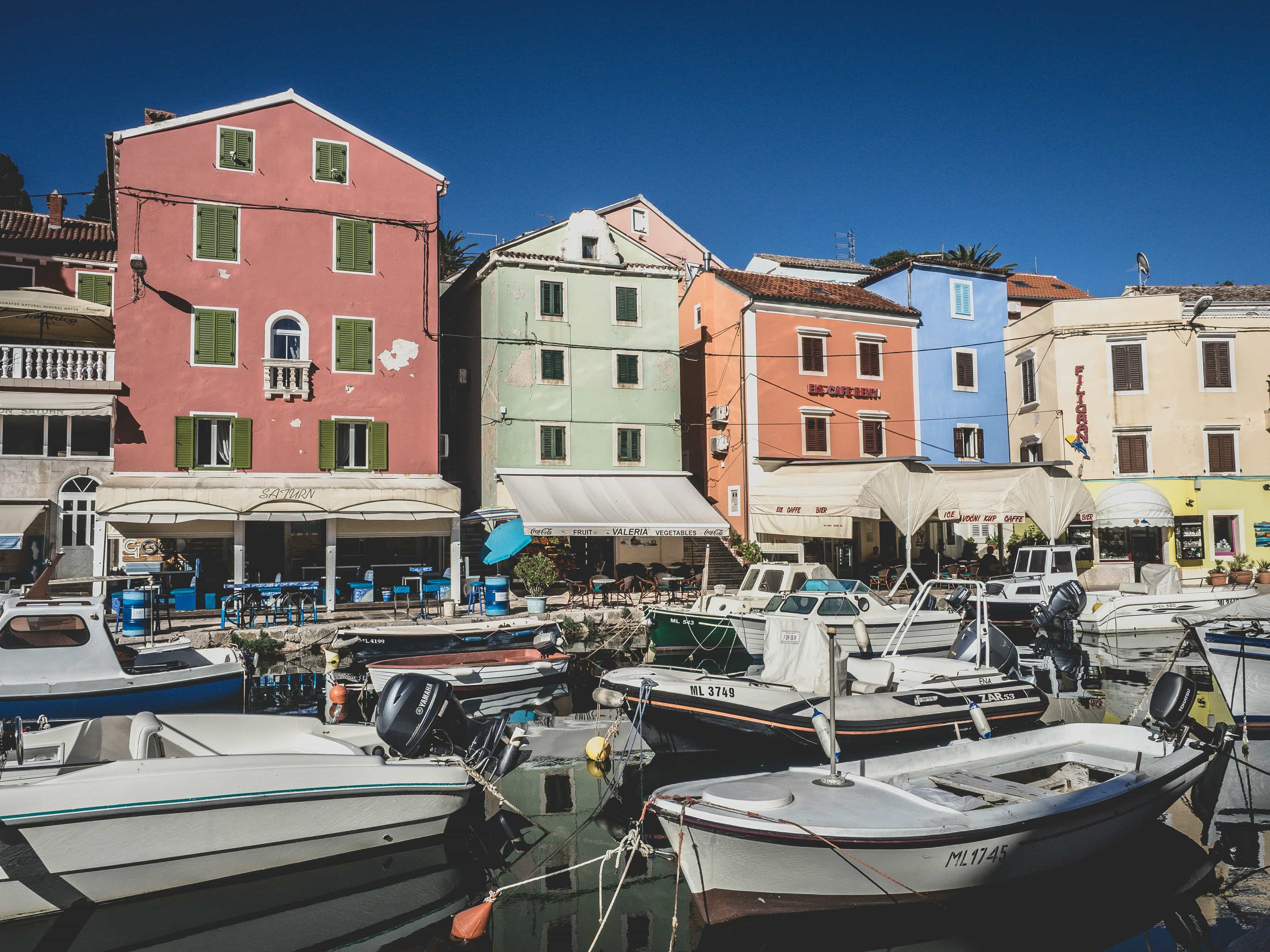 A picturesque harbor with colorful, typical buildings and boats docked, with restaurants lining the sidewalk