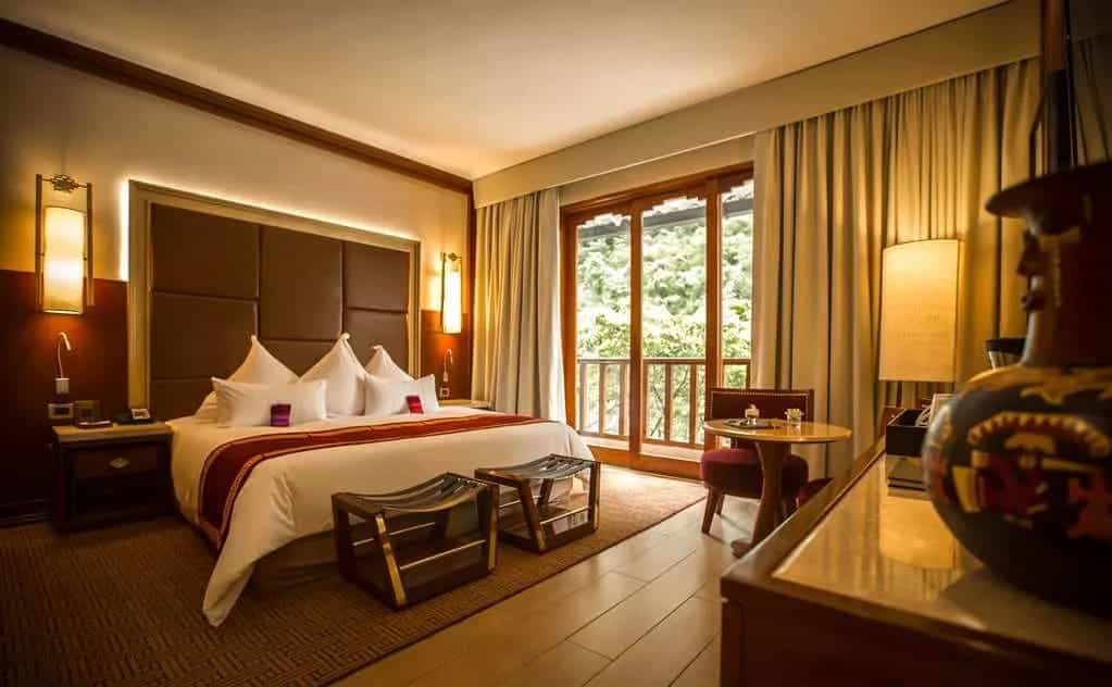 a hotel room with brown headboard, white sheet covered bed, red blanket and wood accents
