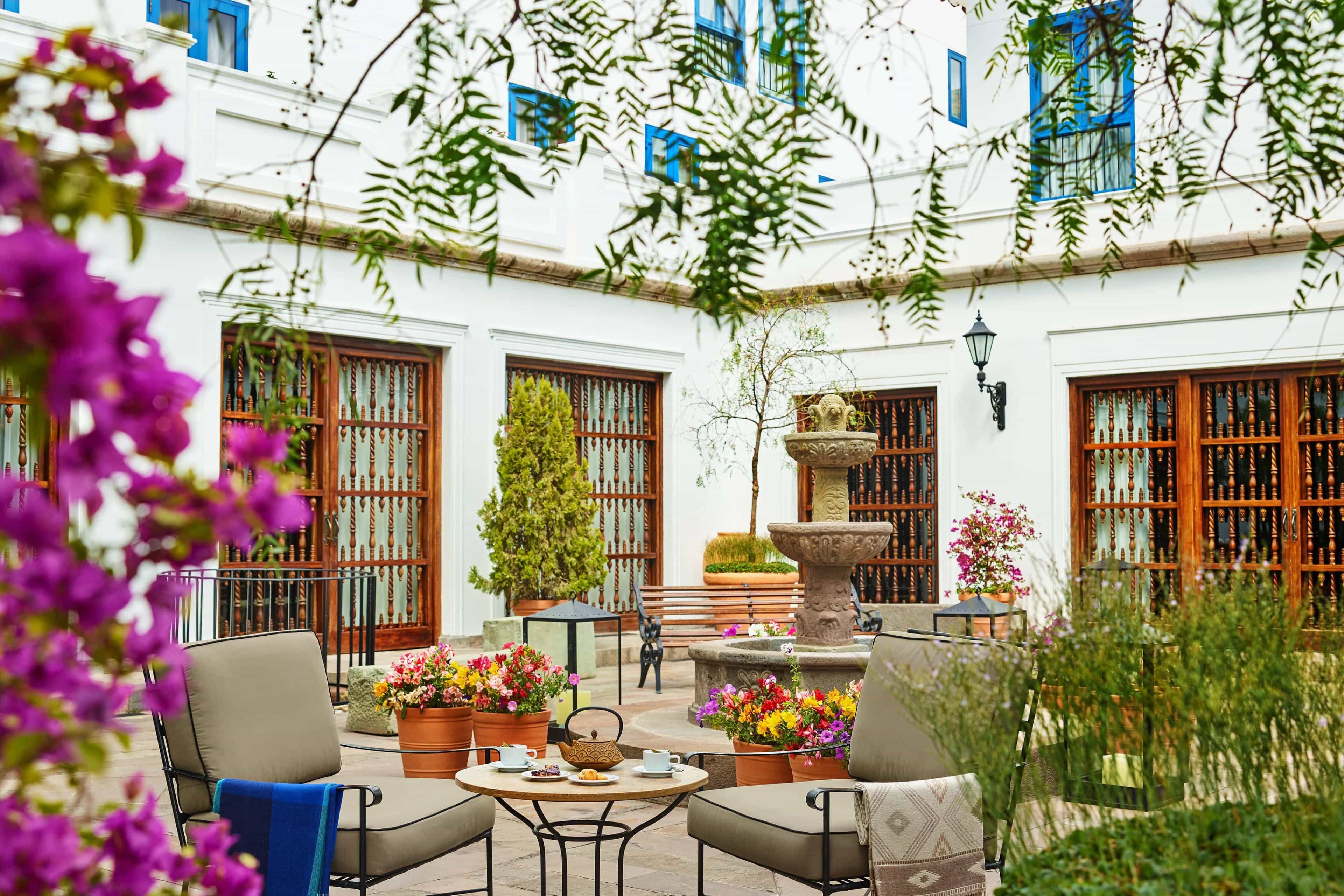 A courtyard of a white stone building with table and chairs, a fountain and potted plants