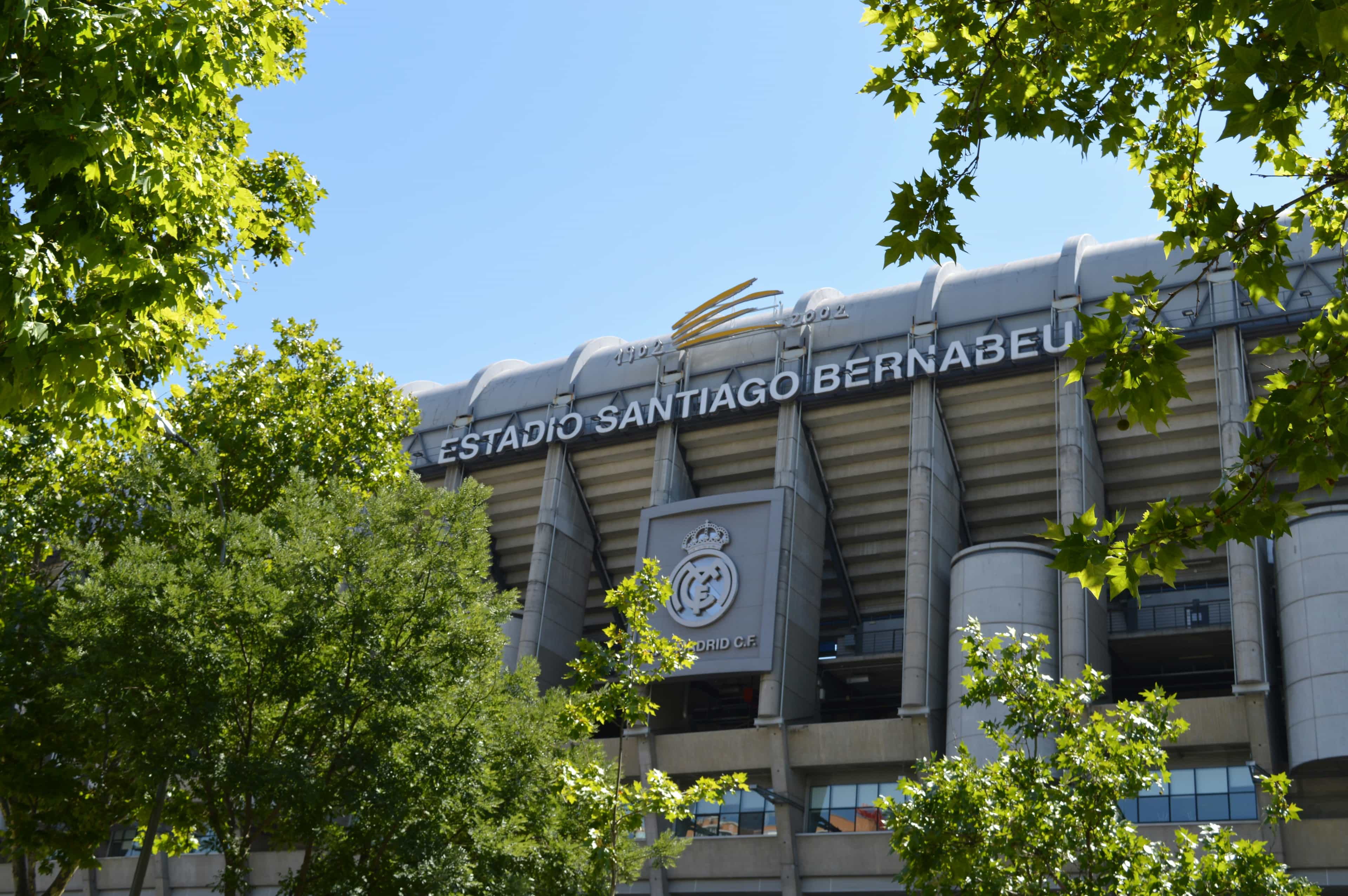 The grey exterior of Estadio Santiago Bernabeu with signage surrounded by foliage