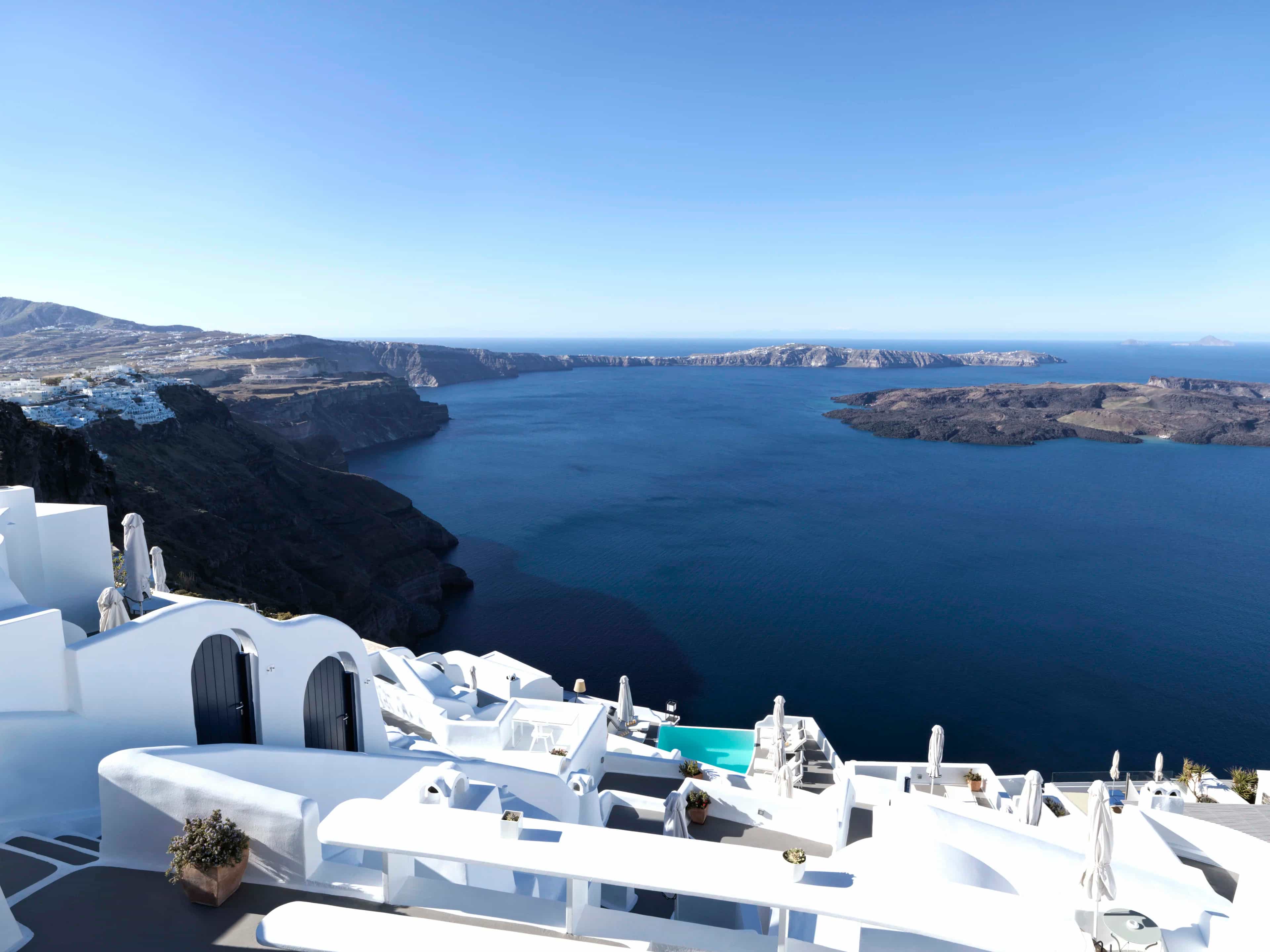 rooftops of white buildings on the edge of a cliff with blue ocean water during day