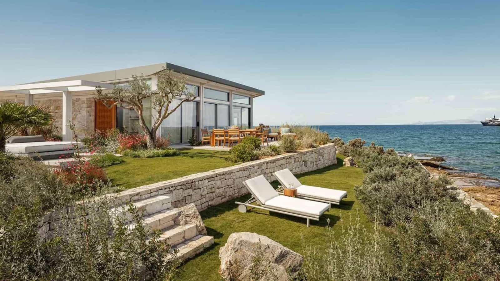 chaise loungers on terraced green grass next to the ocean and in front of a bungalow during day
