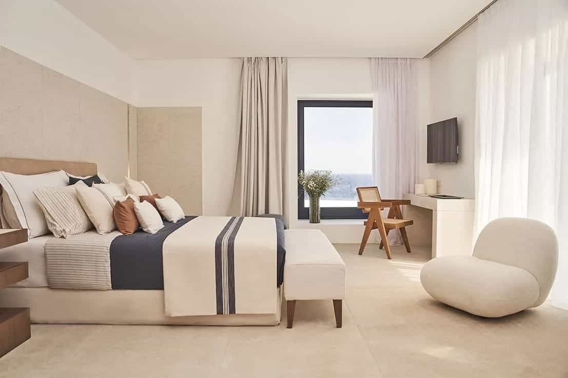 Side view of a white hotel room with white linens and white chair, blue blanket and brown wood accents