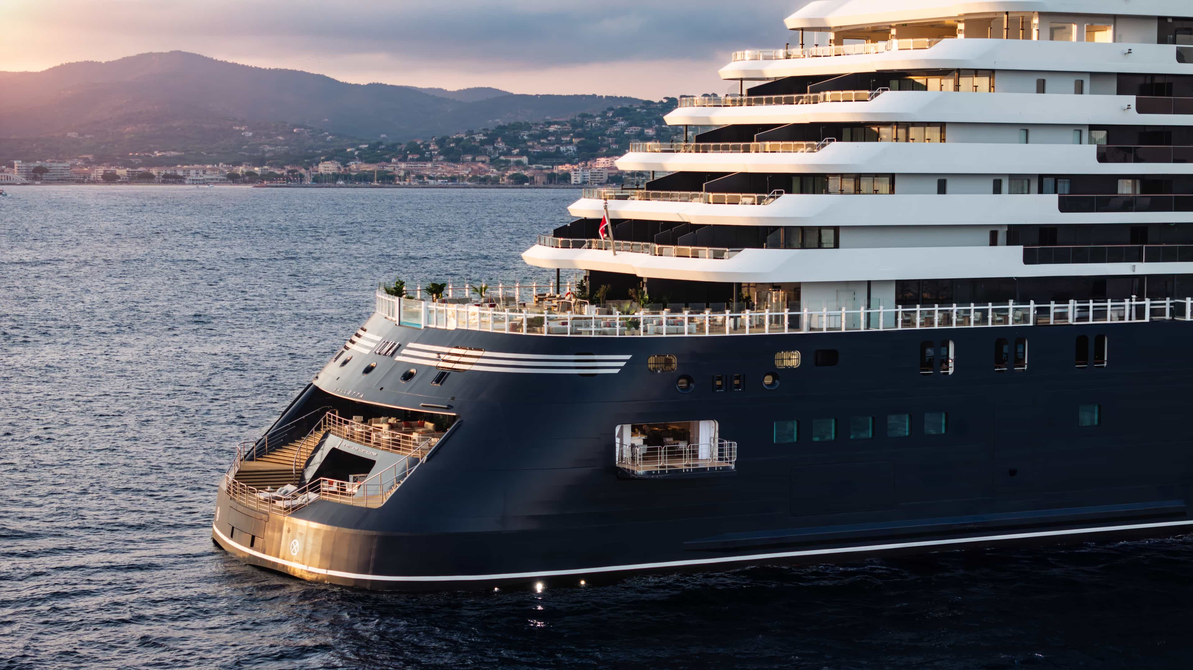 The back of a yacht cruise ship at dusk with mountains in the distance