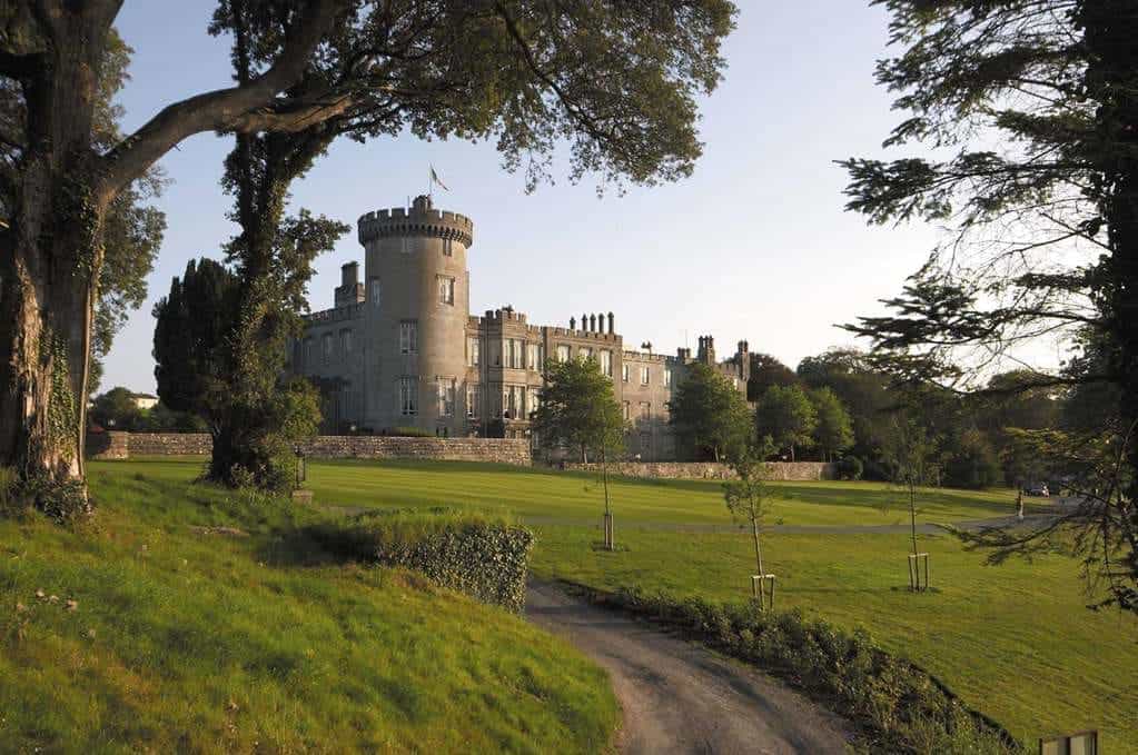 A dirt path with green grass and trees leading to a castle in daytime