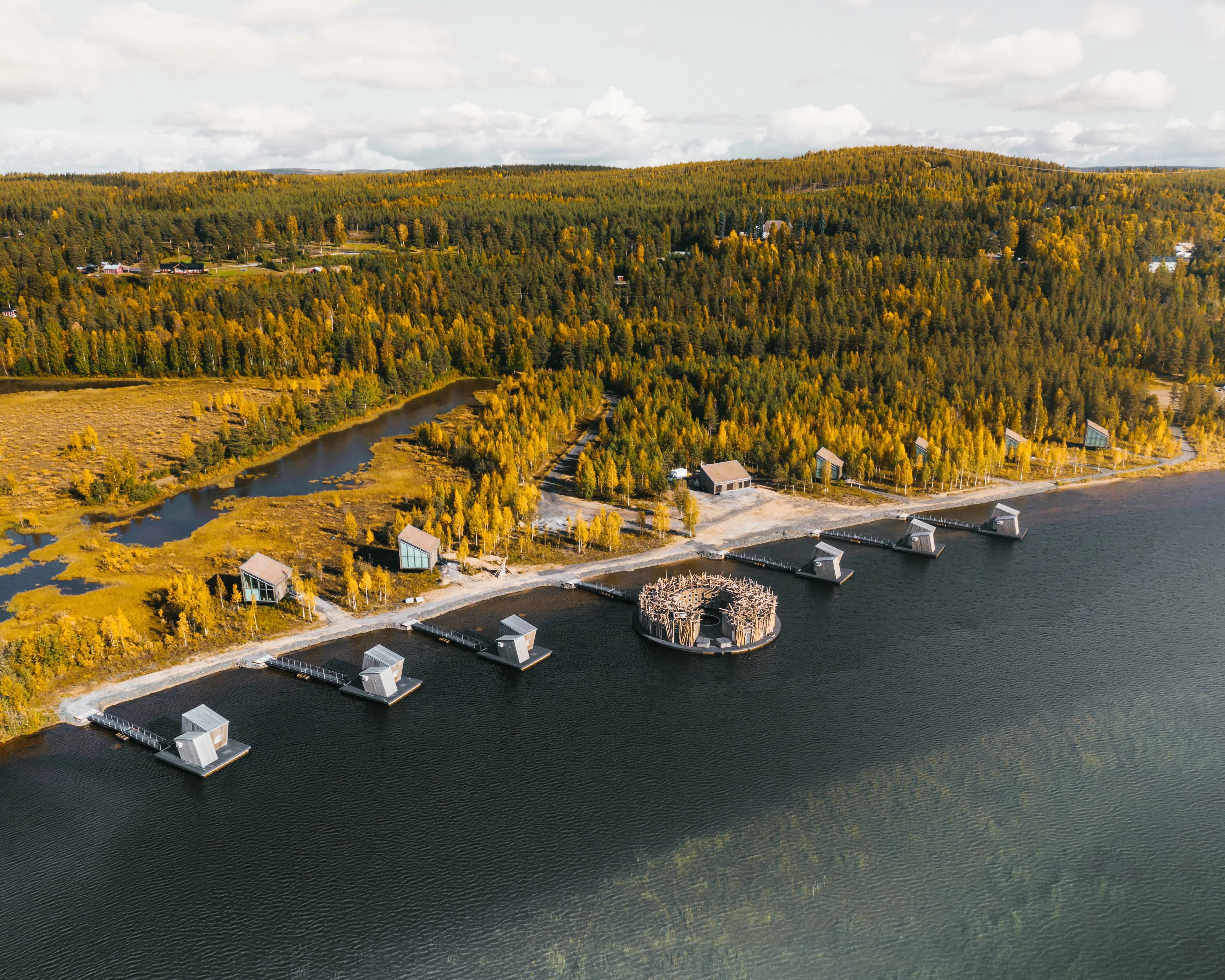 cabins floating on a river and on the riverbank with fall foliage forest behind during day