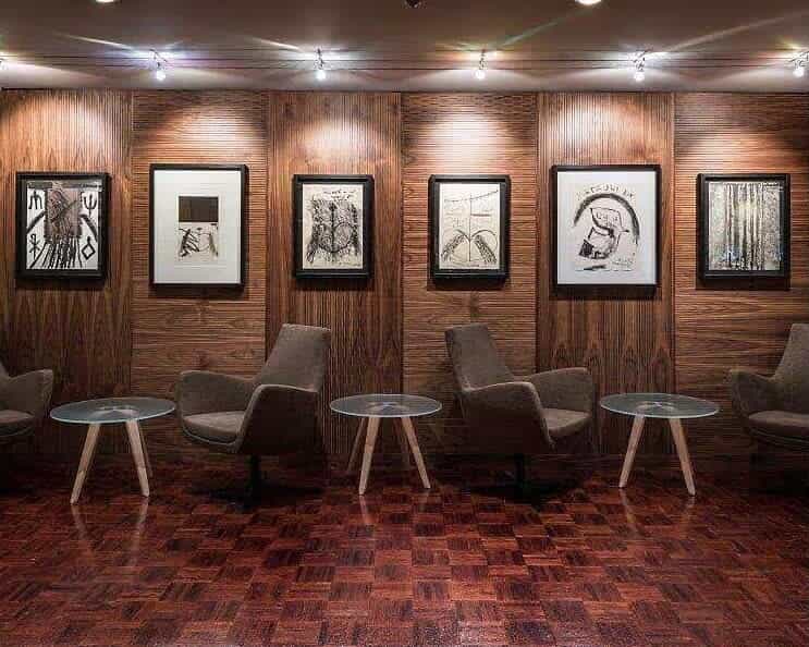brown wood wall of illuminated artwork with side tables and chairs under