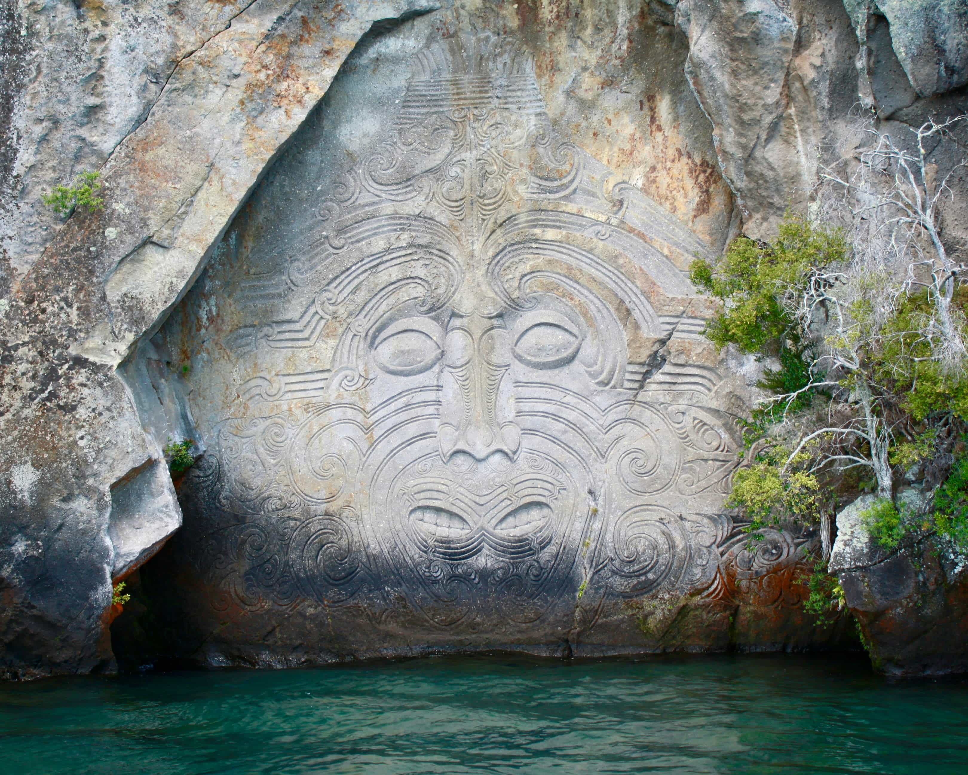 Maori rock carvings with green vegetation and turquoise water